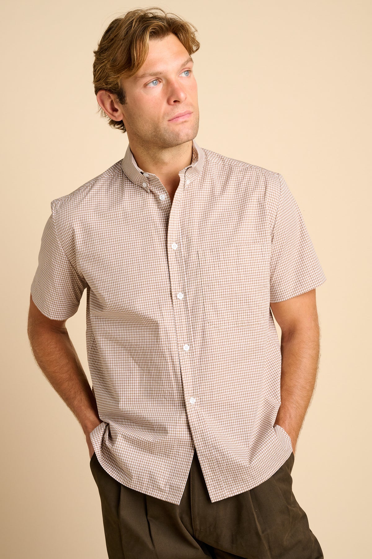 Man wearing a short-sleeve checkered shirt against a beige background.