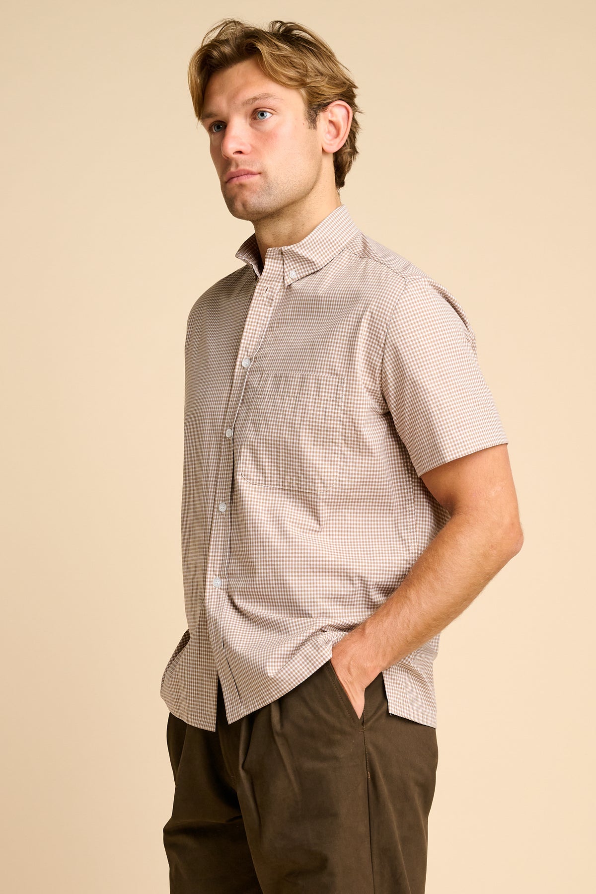 Man wearing a short-sleeve checkered shirt against a beige background.