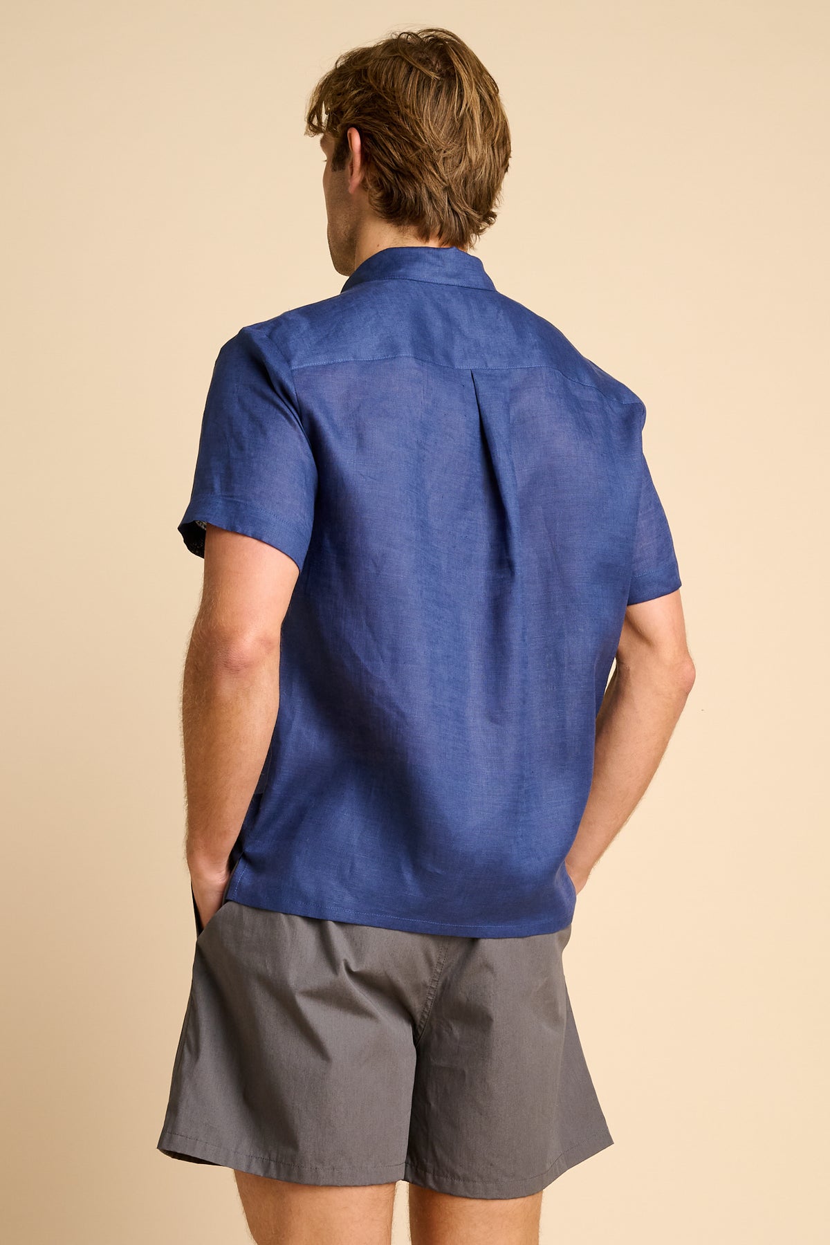 Man wearing a blue shirt and grey shorts on a beige background.