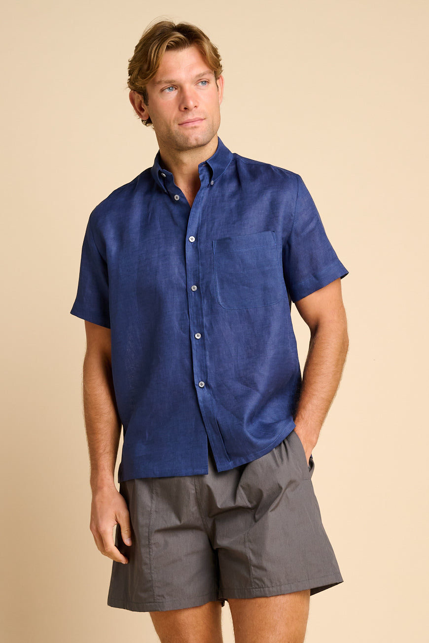 Man wearing a blue shirt and grey shorts on a beige background.