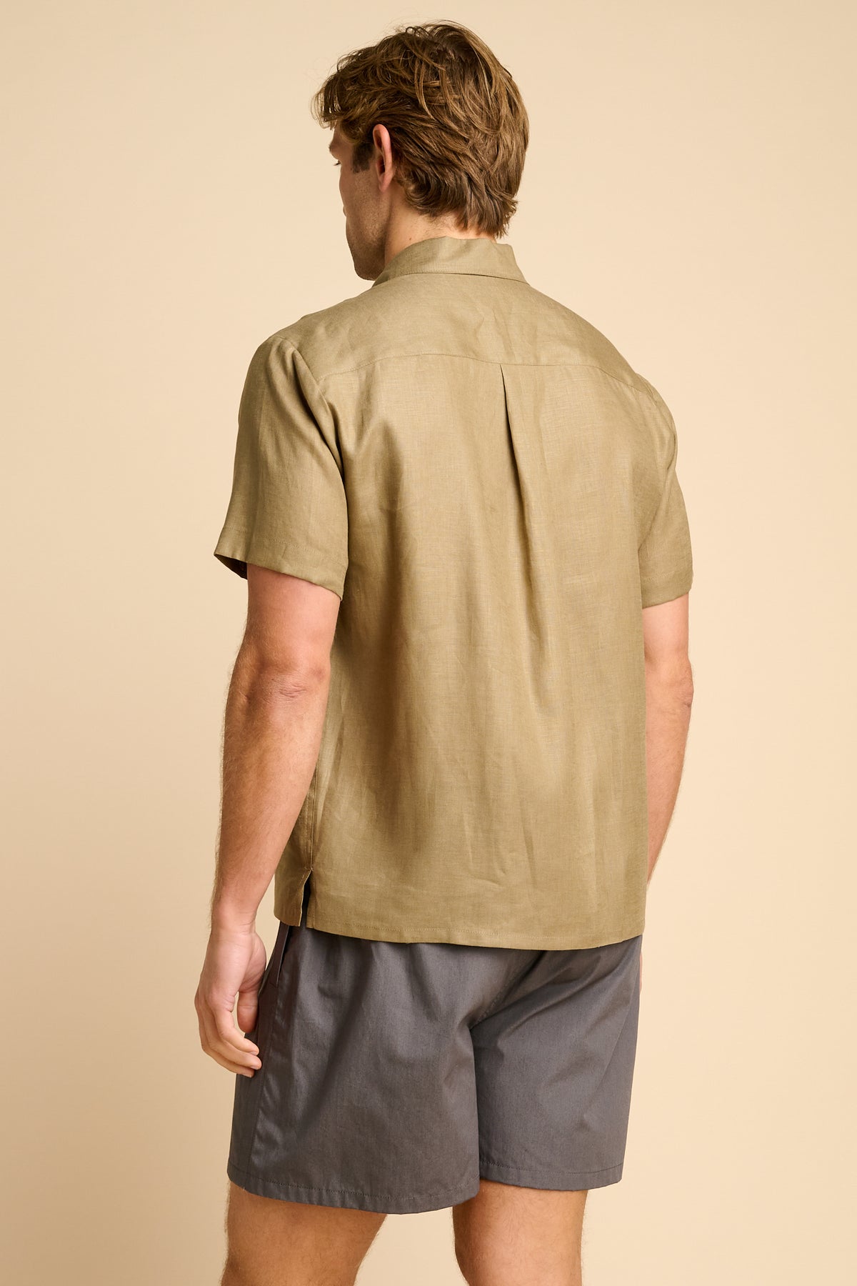Man wearing a olive short-sleeve shirt and grey shorts on a beige background