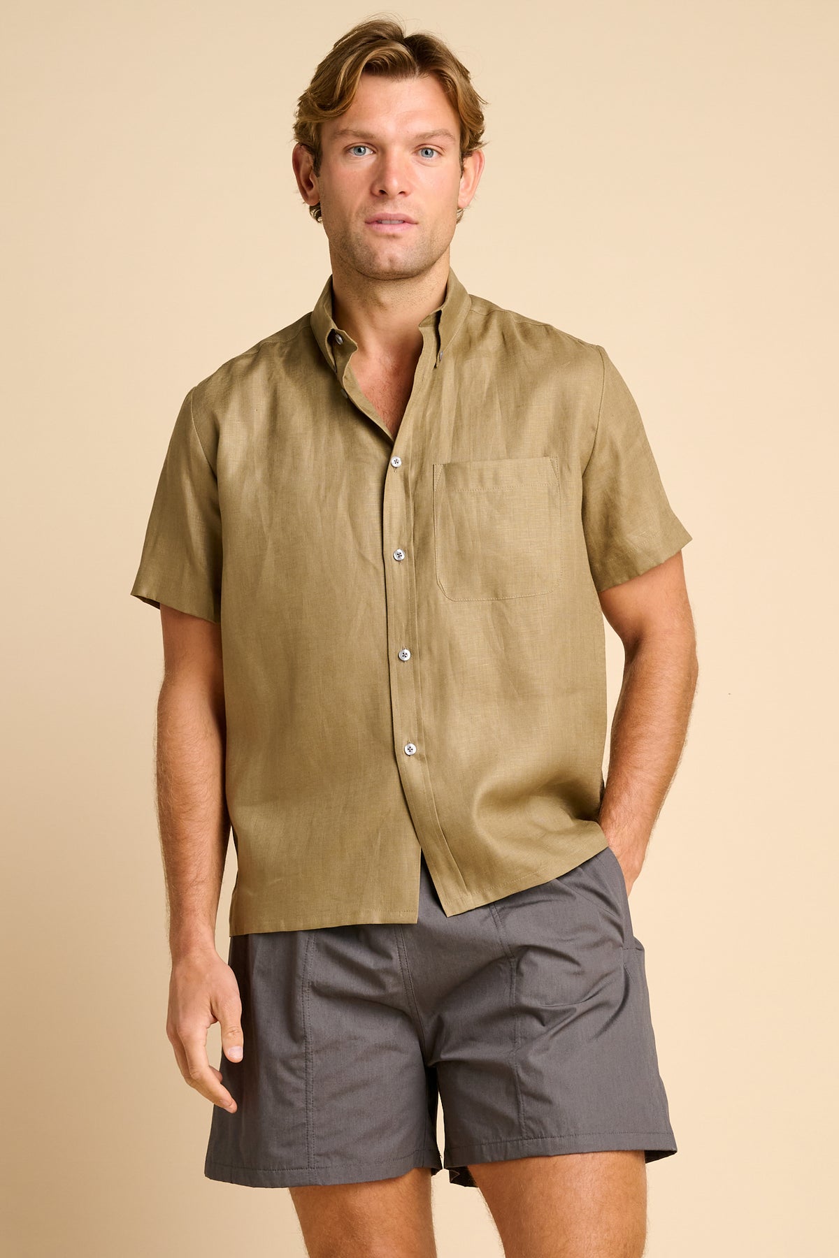 Man wearing a olive short-sleeve shirt and grey shorts on a beige background