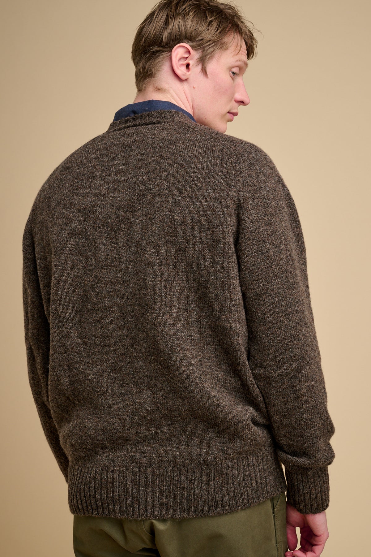 The back of man wearing a brown sweater against a beige background.
