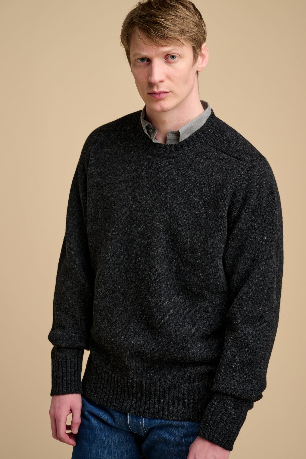 Man wearing charcoal marl knit jumper on beige background.