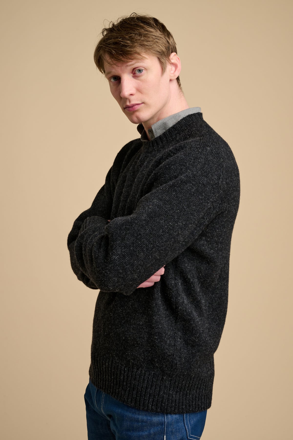 Man wearing charcoal marl knit jumper on beige background.