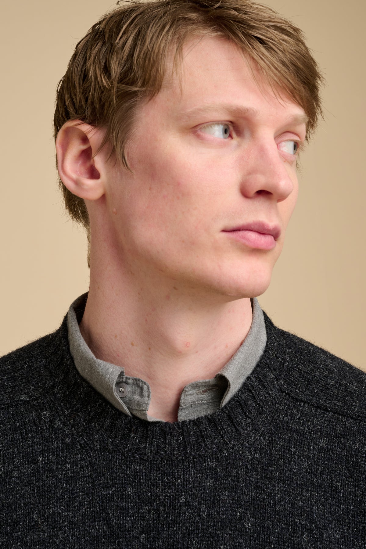 Man wearing charcoal marl knit jumper on beige background.