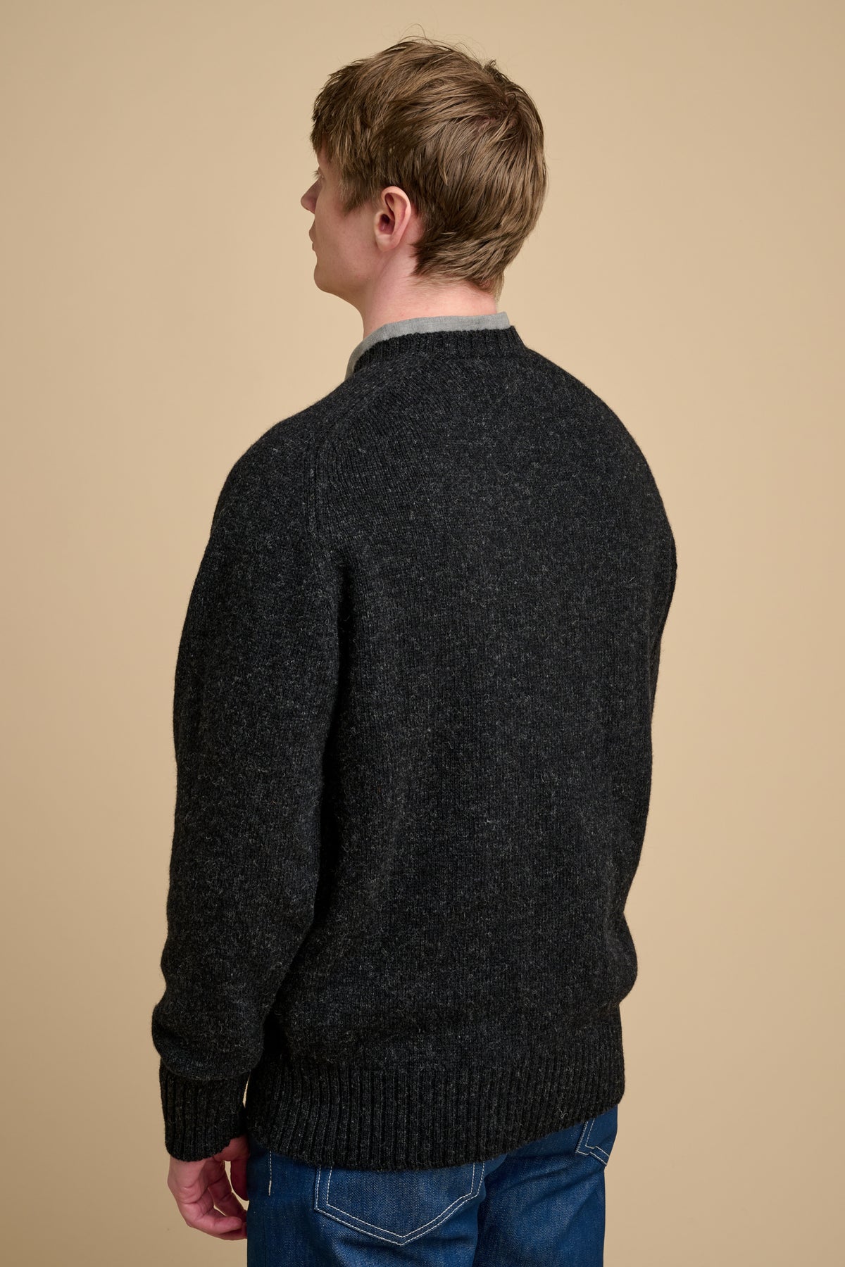 The back of man wearing charcoal marl knit jumper on beige background.