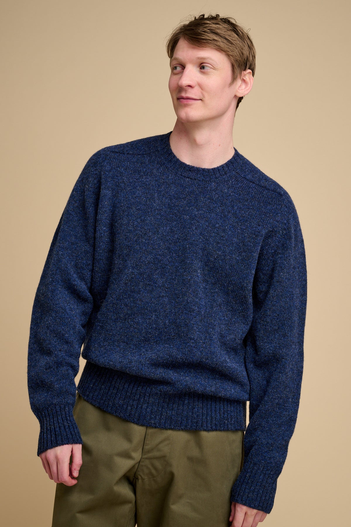 Man wearing a blue Knit jumper against a beige background.