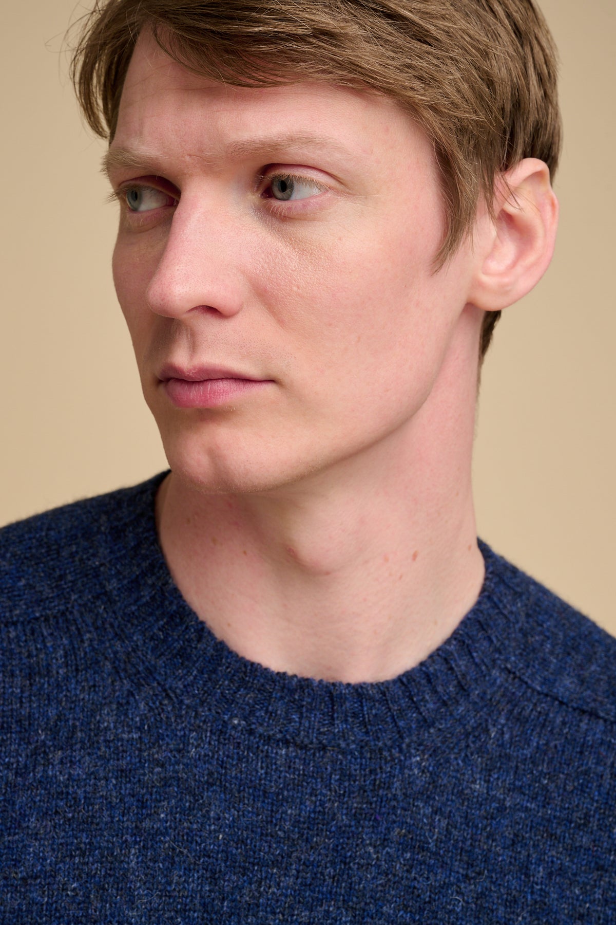 Close-up of a man wearing a blue sweater against a beige background
