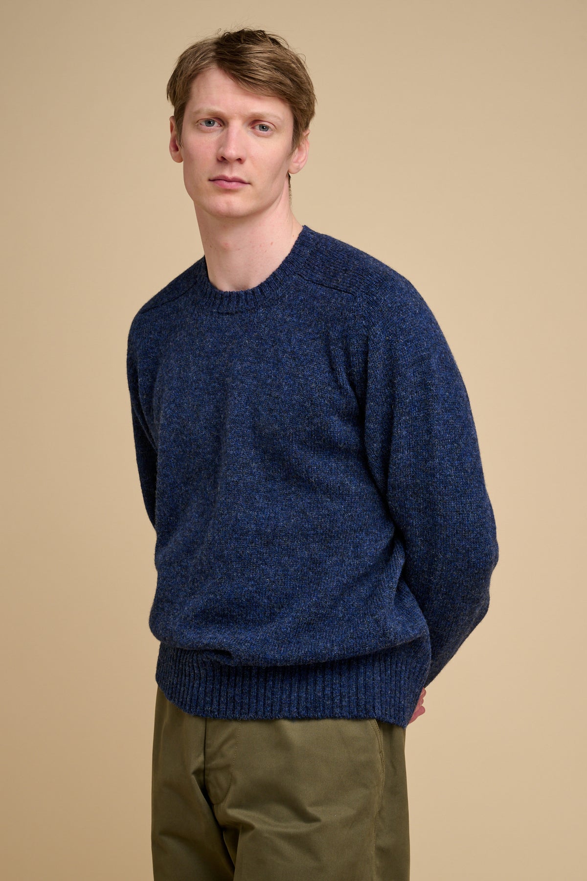 Man wearing a blue Knit jumper against a beige background.