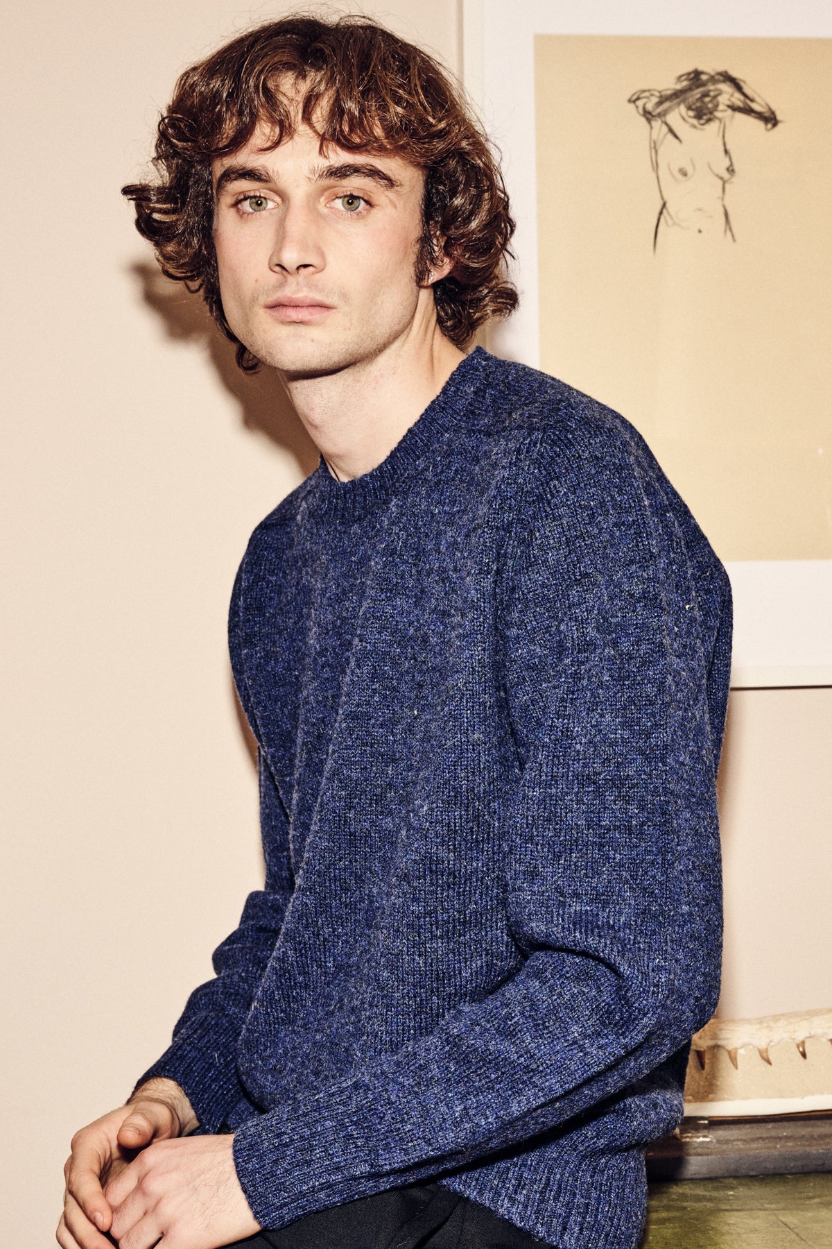 Man wearing a blue shetland jumper sitting in a room with a neutral background.