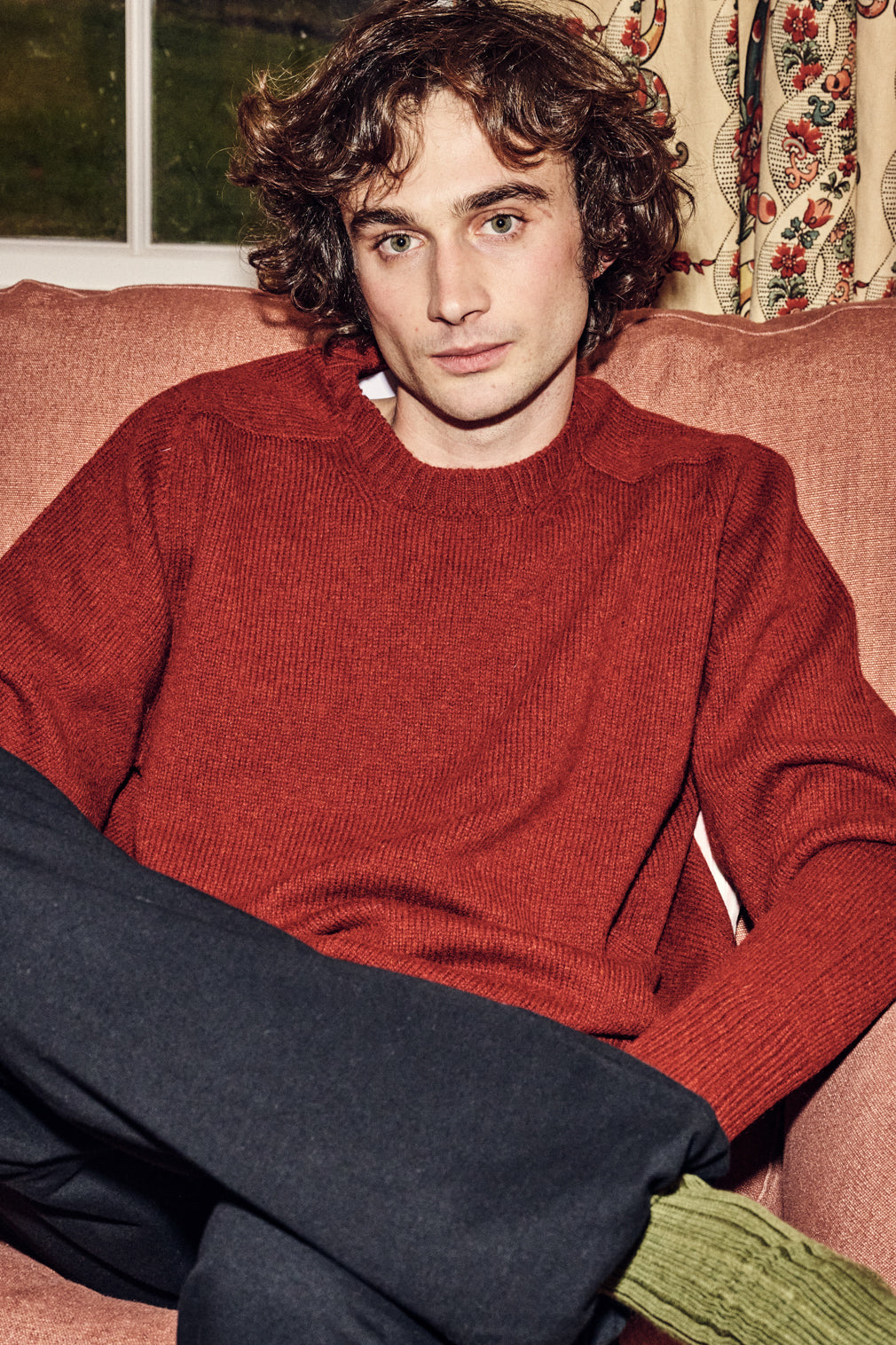 Male sat on sofa wearing red jumper and black sweatpants