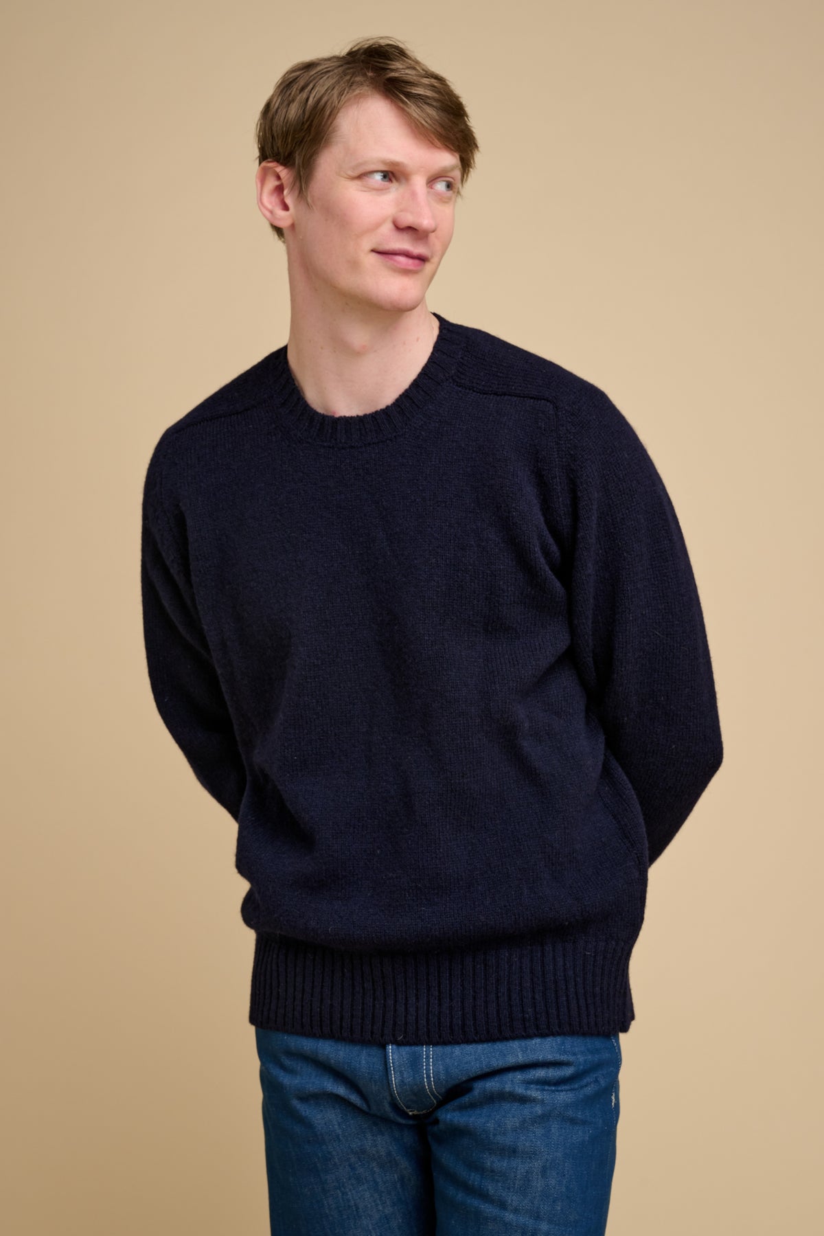 Man wearing a navy knit sweater and jeans against a beige background