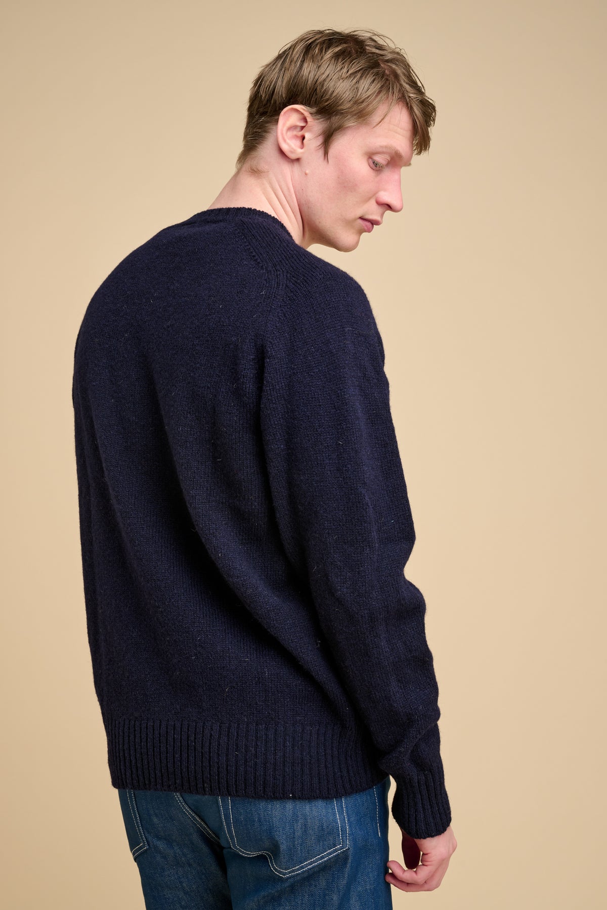 Man wearing a navy sweater and blue jeans against a beige background
