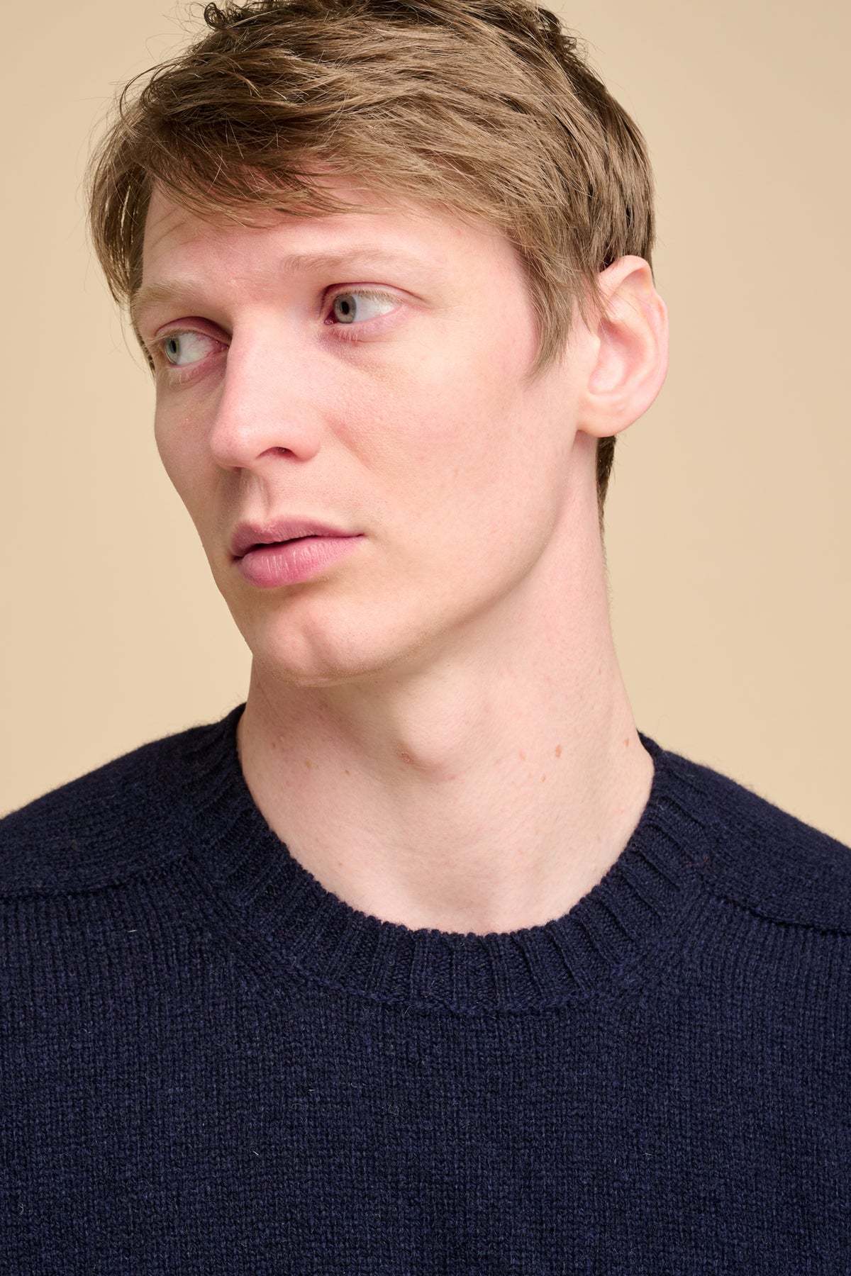 Close up of a man wearing a navy sweater against a beige background