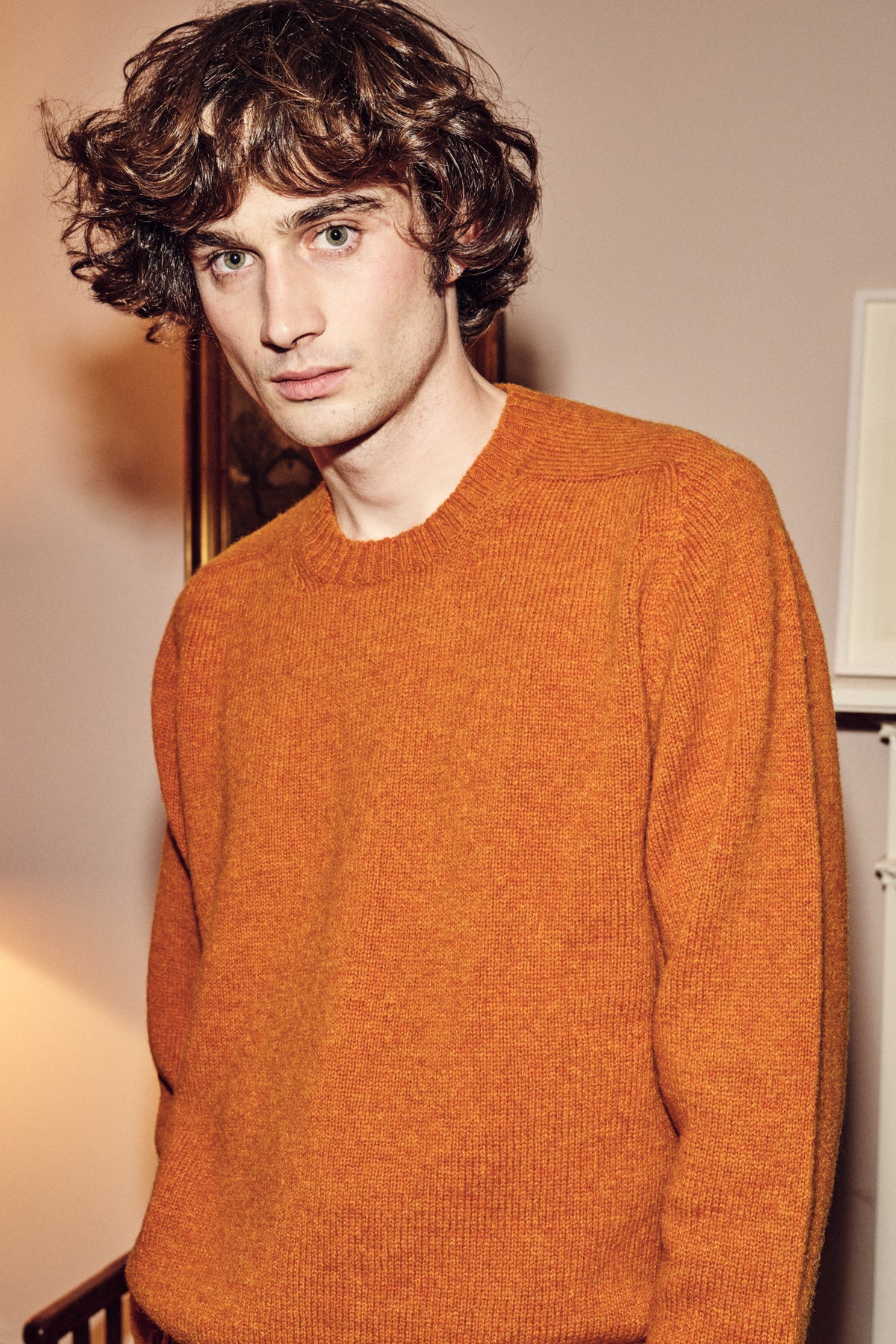 Man wearing an orange sweater indoors with a neutral background