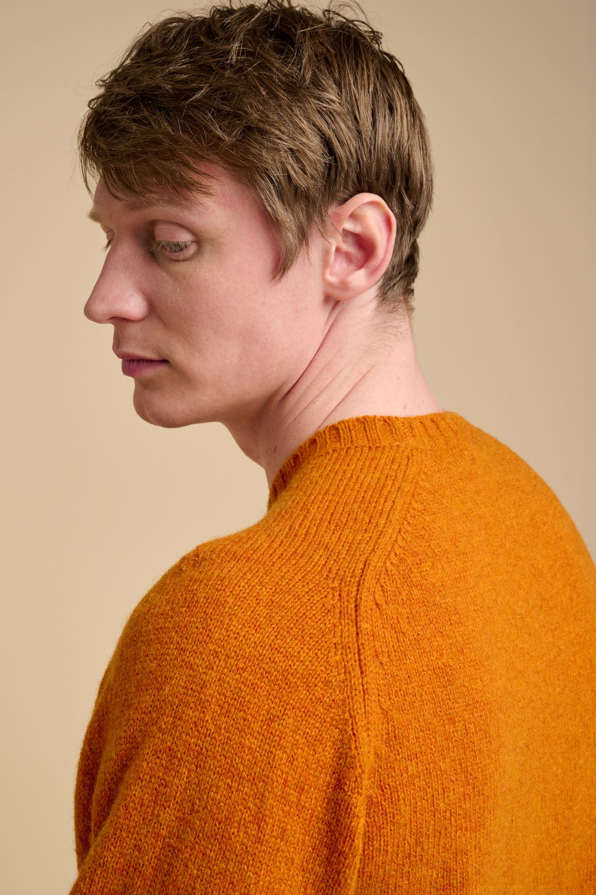 Person wearing an orange sweater against a beige background