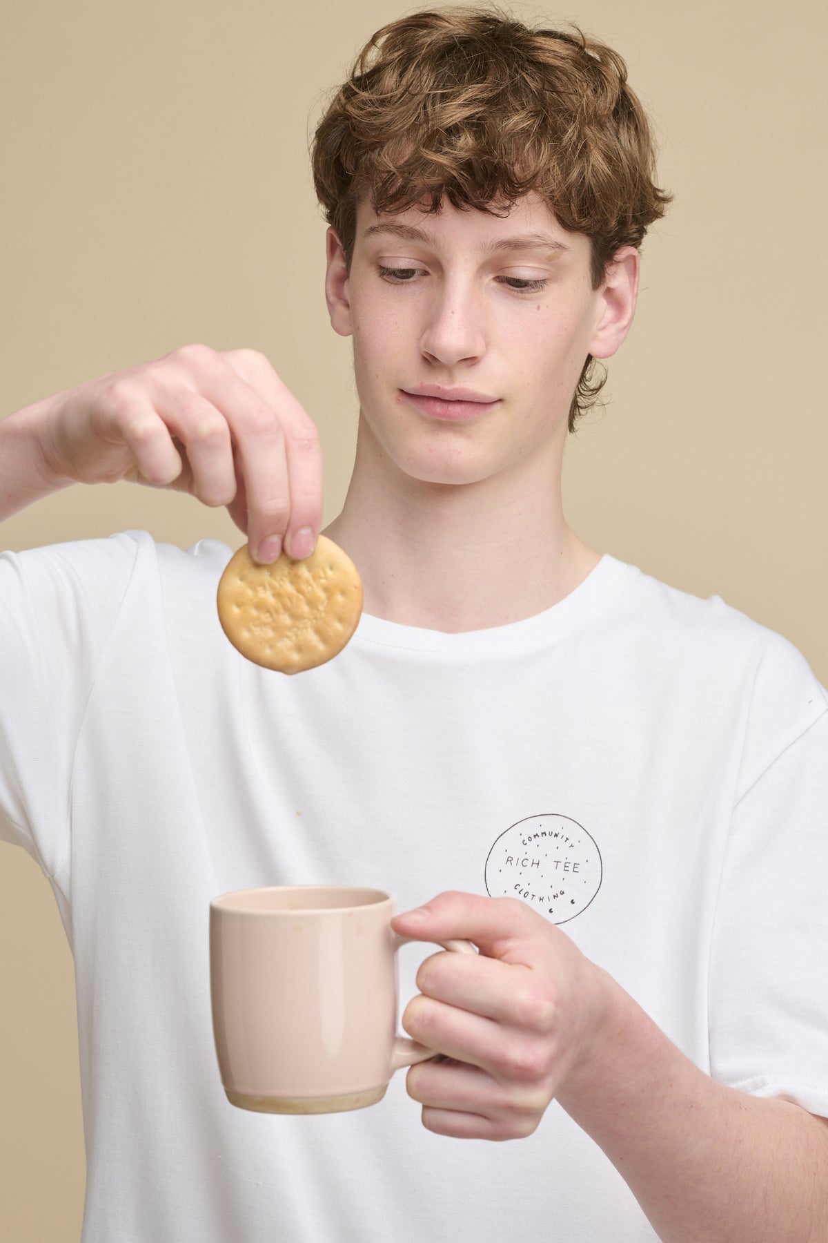 Portrait of male holding a rich tea biscuit dipped into a mug of tea wearing short sleeve graphic t shirt with rich tee biscuit print, holding a rich tea biscuit.