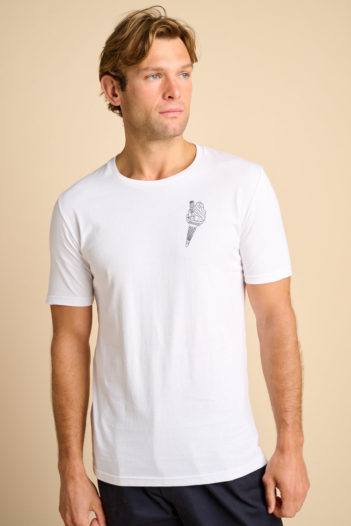 A man wearing a white short-sleeve crew neck t-shirt with a small ice cream cone graphic on the left of chest, set against a solid beige background.