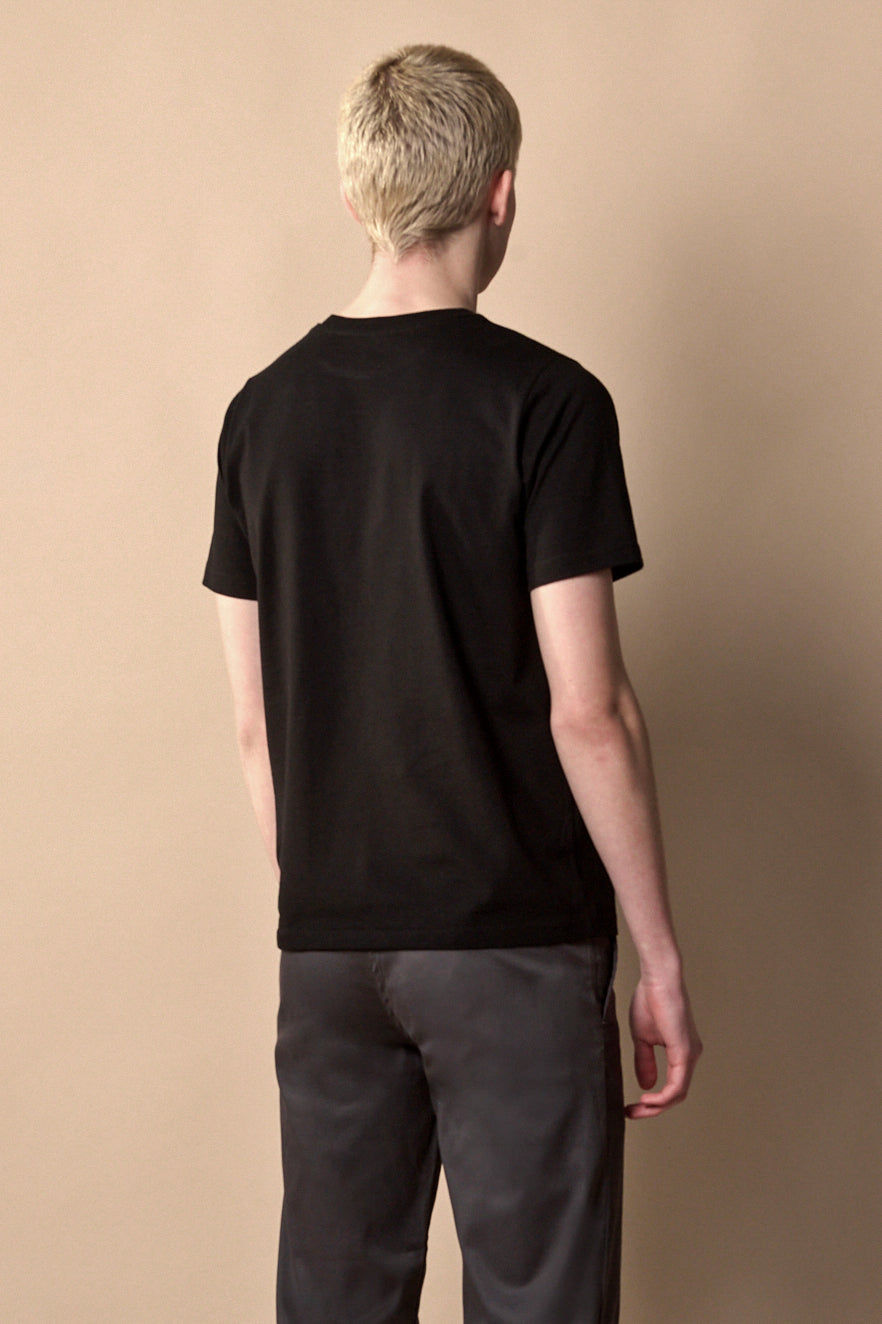 Thigh up front of male with short blond hair wearing short sleeve t-shirt in black.