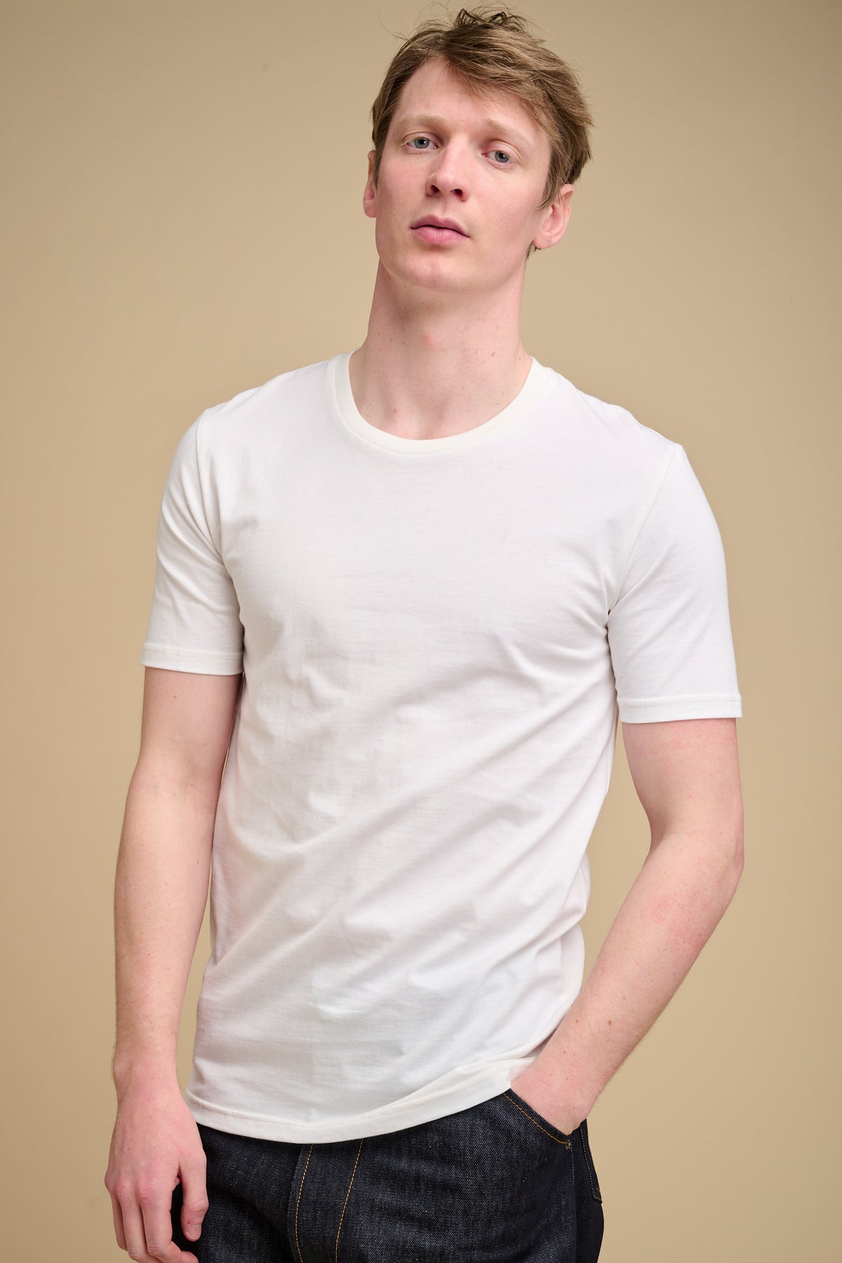 Man wearing a bone t-shirt against a beige background.