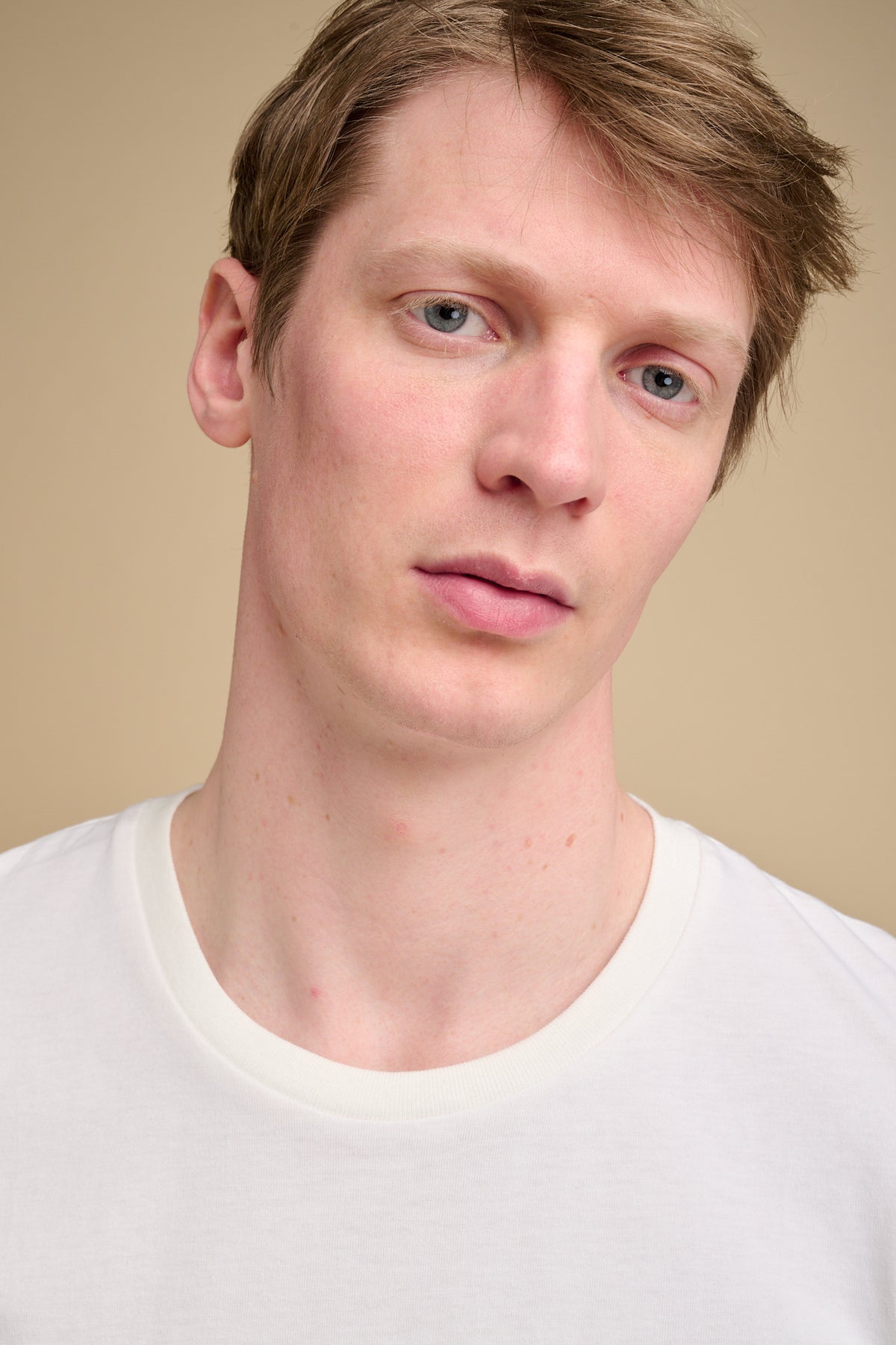 Man wearing a bone t-shirt against a beige background.