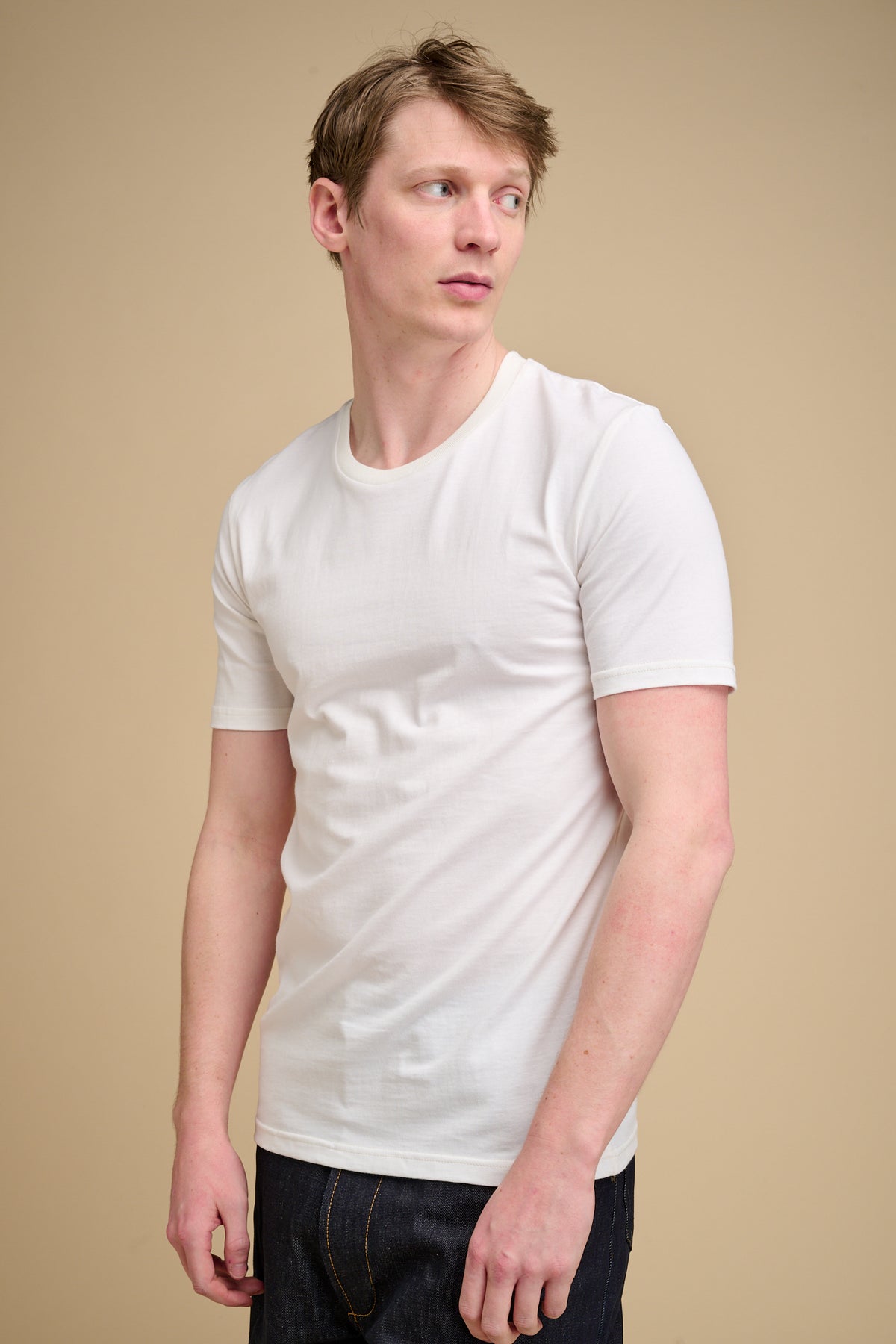 Man wearing a bone t-shirt against a beige background.