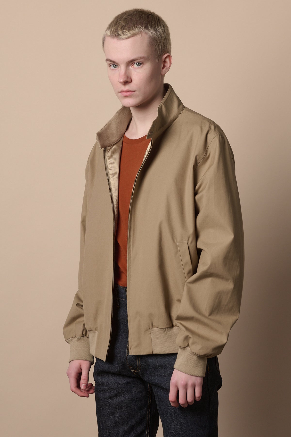 male wearing cinnamon short sleeve t shirt under men's harrignton jacket in stone paired with indigo jeans 