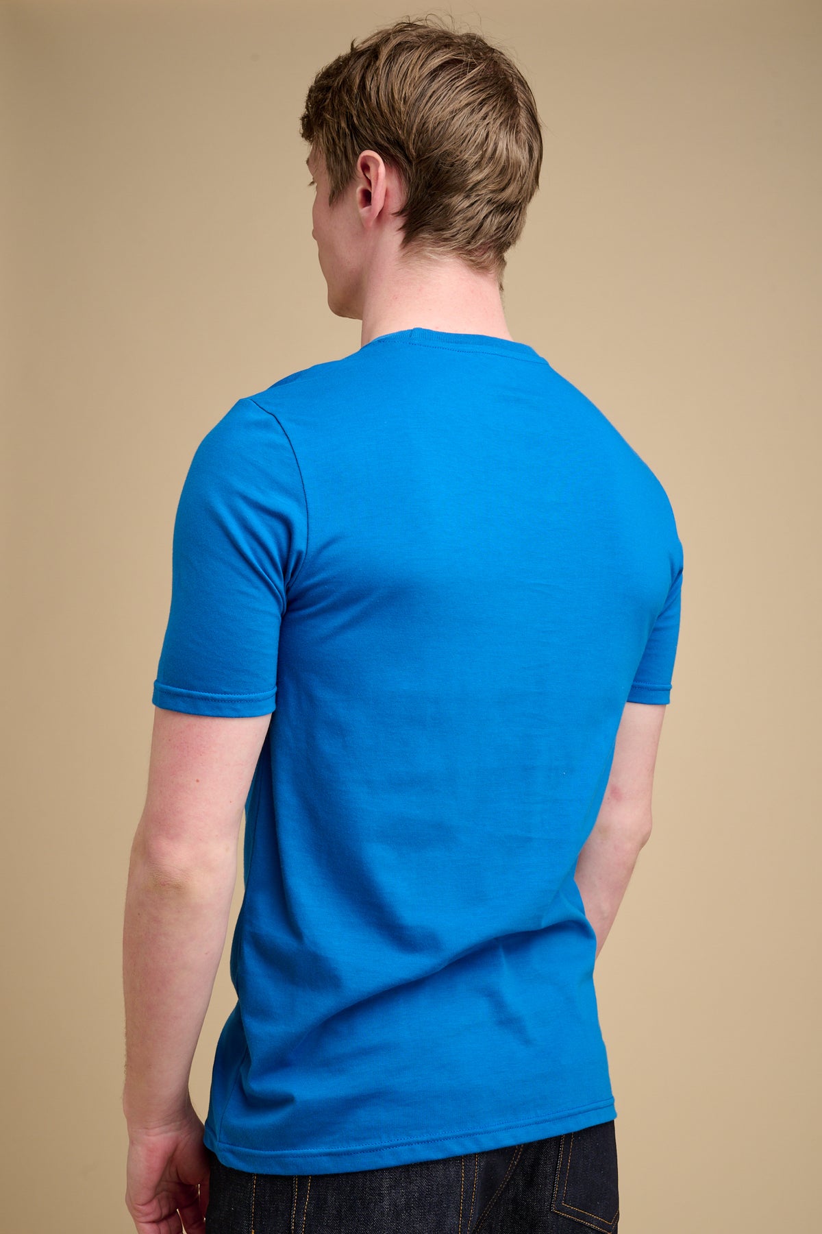 The back of man wearing cobalt blue t shirt against beige background.