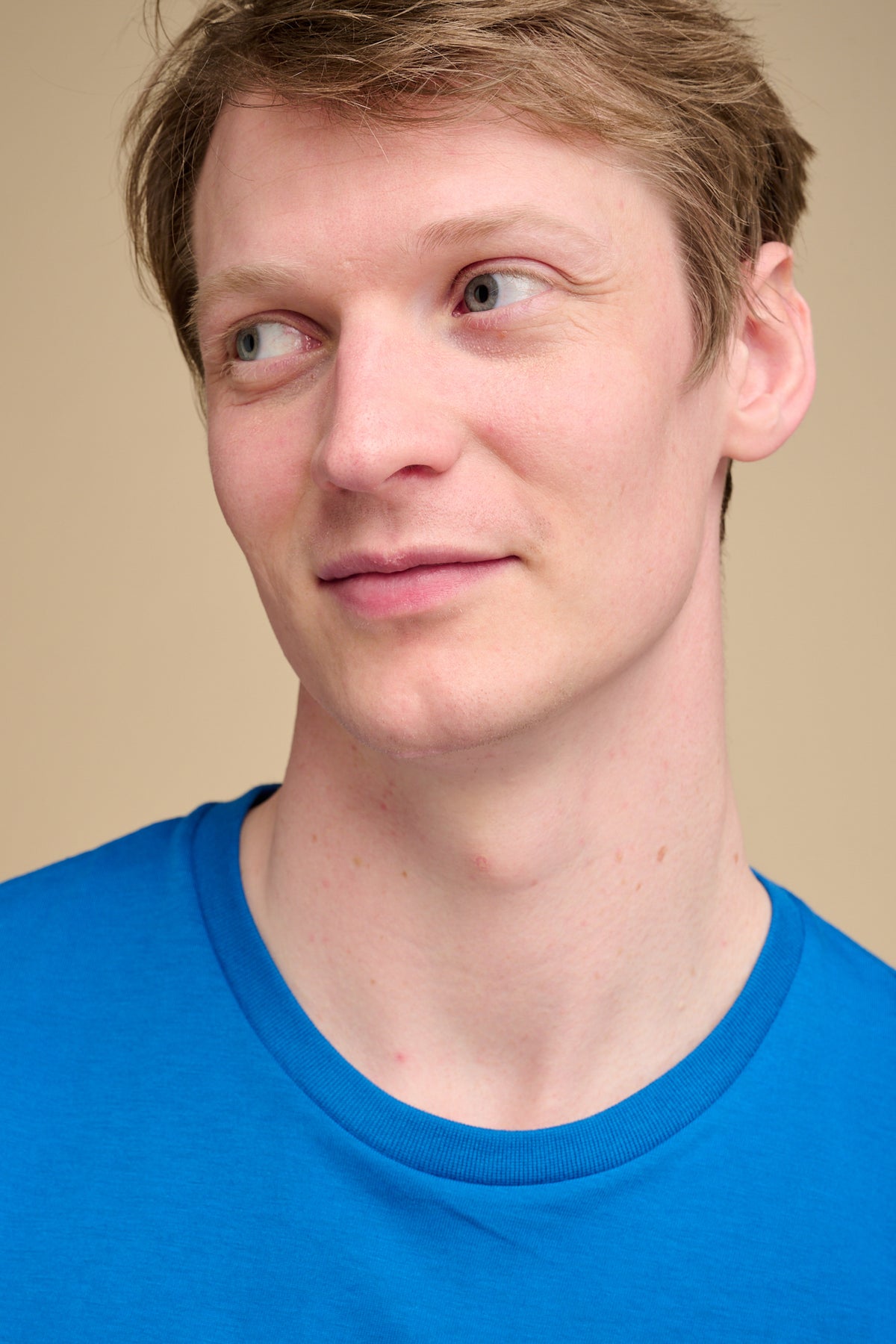 Man wearing cobalt blue t shirt against beige background.