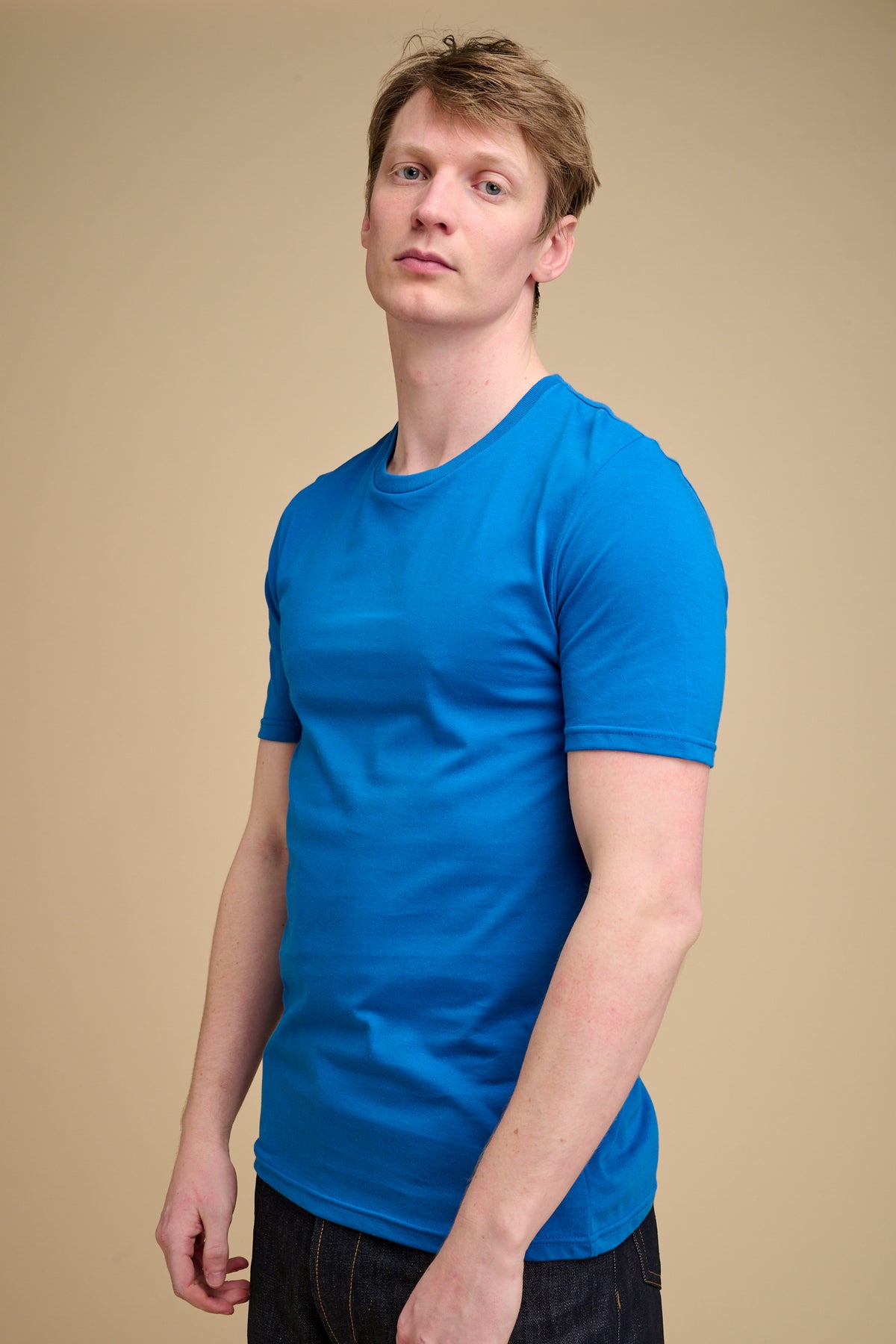Man wearing cobalt blue t shirt against beige background.