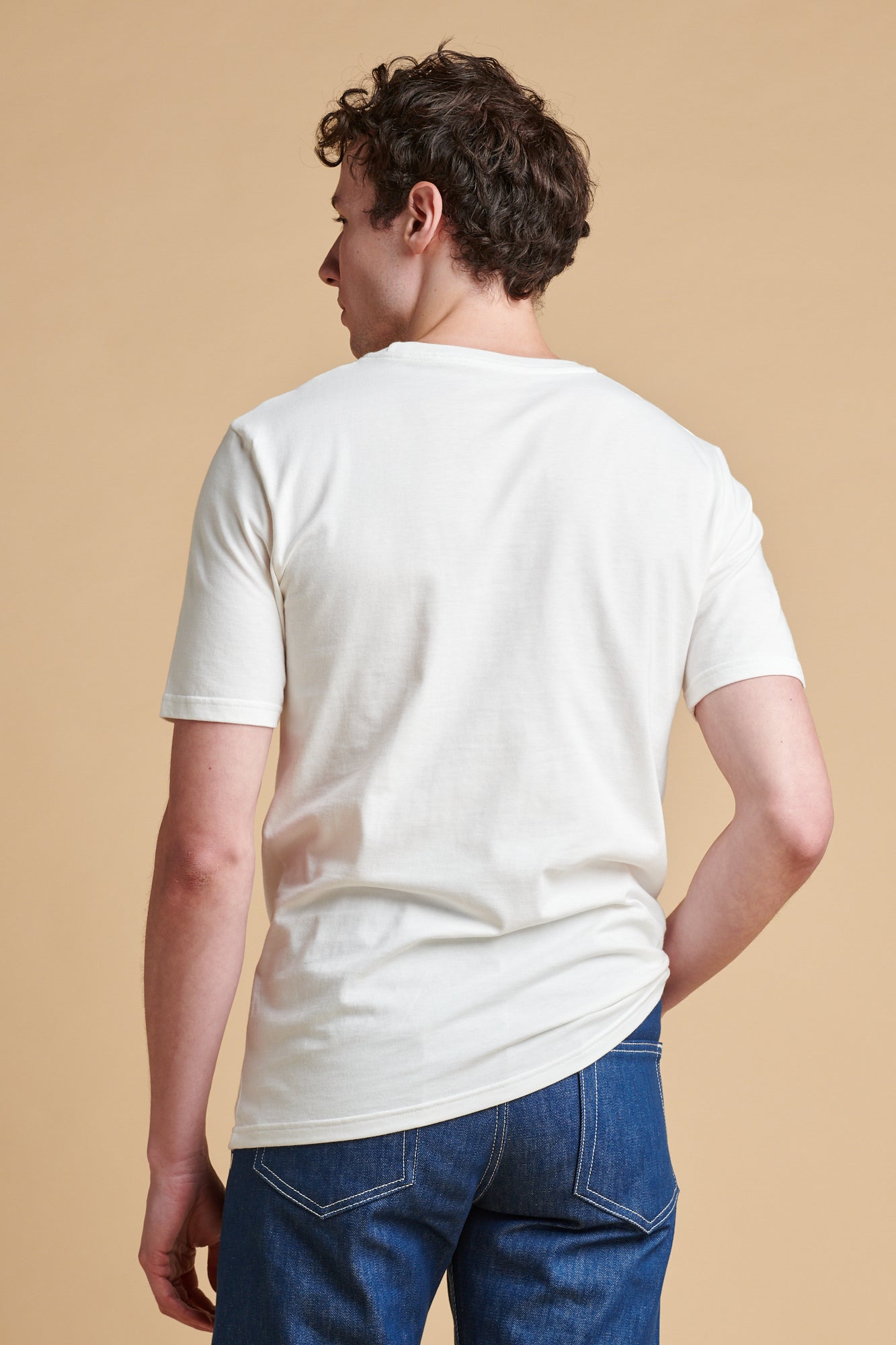 Person wearing a white t-shirt with a small graphic on a beige background