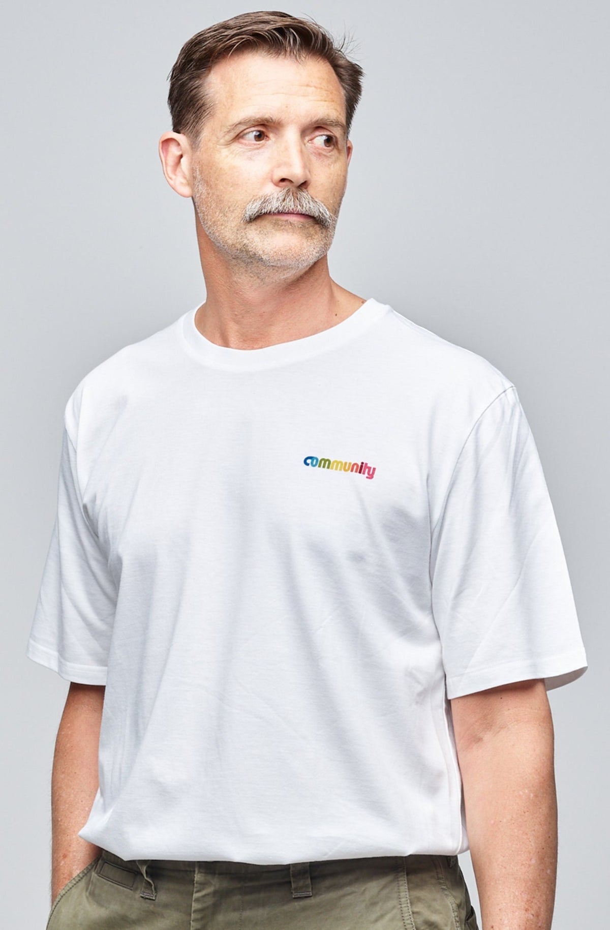 Community Clothing founder, Patrick Grant, wearing a white short sleeve t-shirt with branding on the chest. Styled tucked in