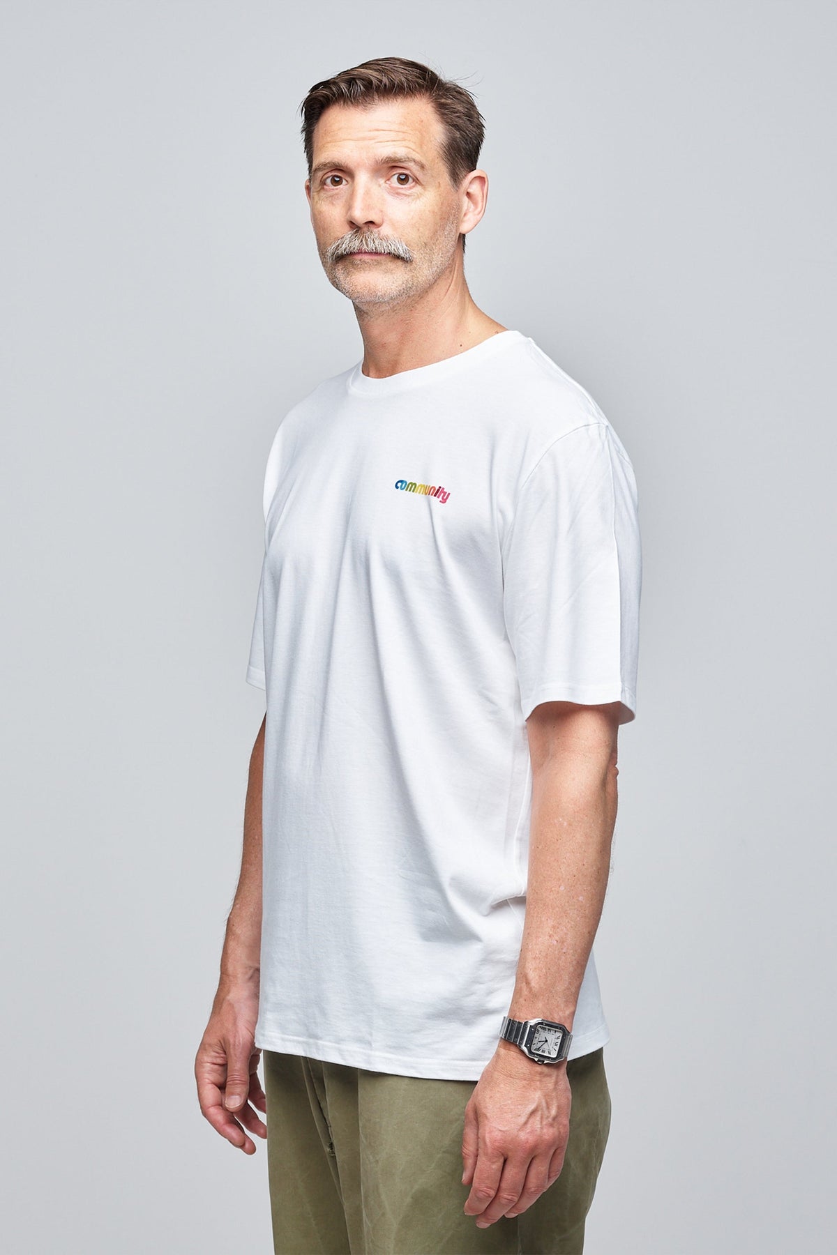 Community Clothing founder, Patrick Grant, wearing a white short sleeve t-shirt with branding on the chest. Styled untucked