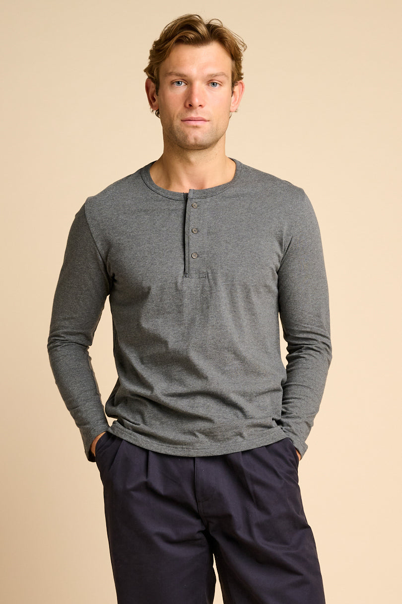Man wearing a grey long-sleeve henley shirt and navy pants on a beige background.