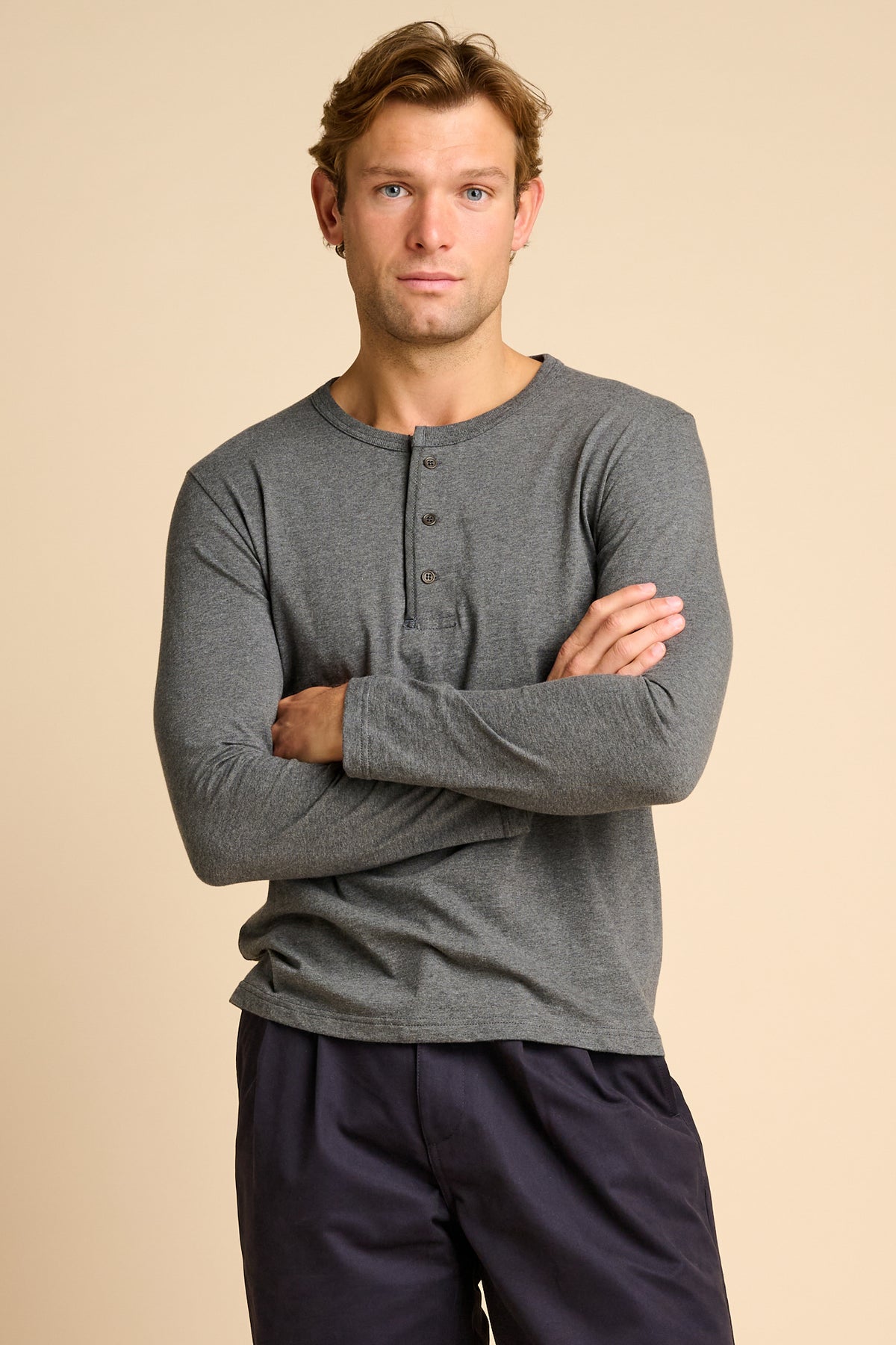 Man wearing a grey long-sleeve henley shirt and dark pants against a beige background.