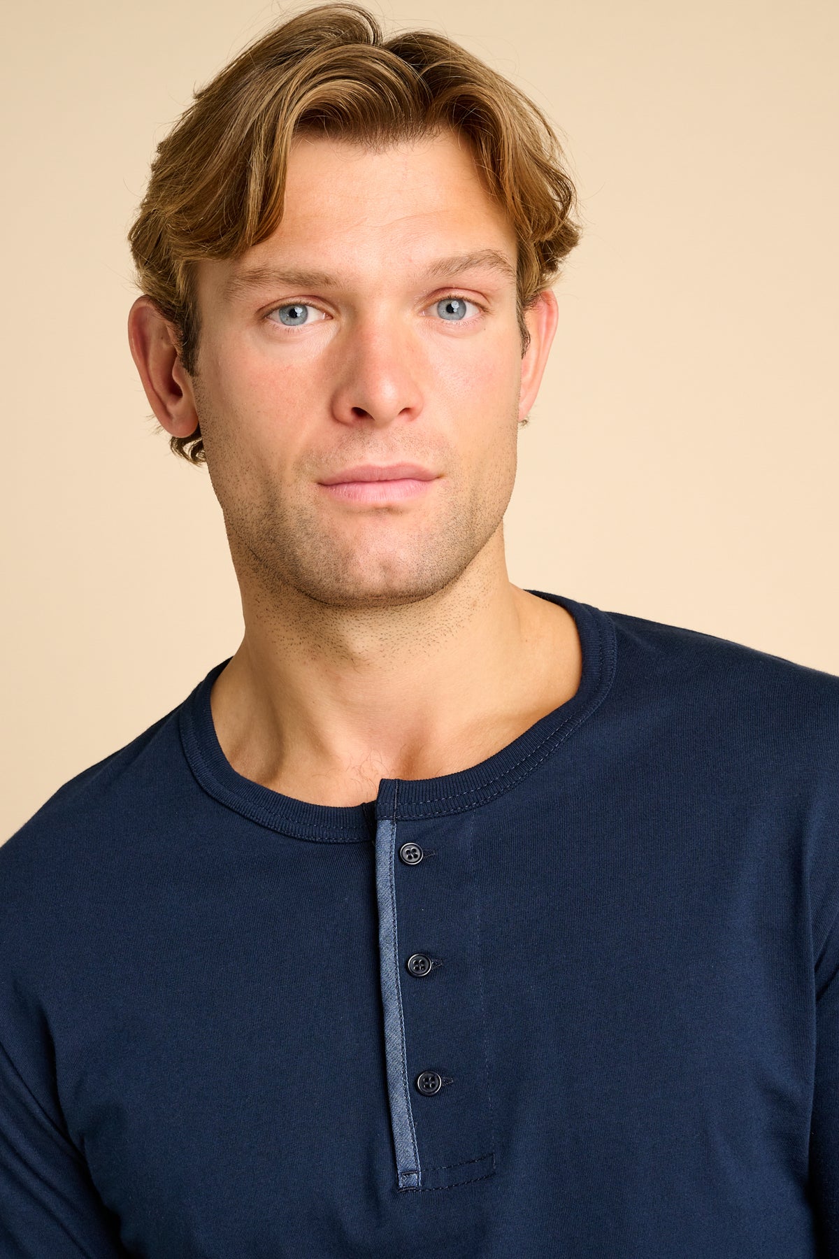 Man wearing a navy blue long-sleeve shirt against a beige background.