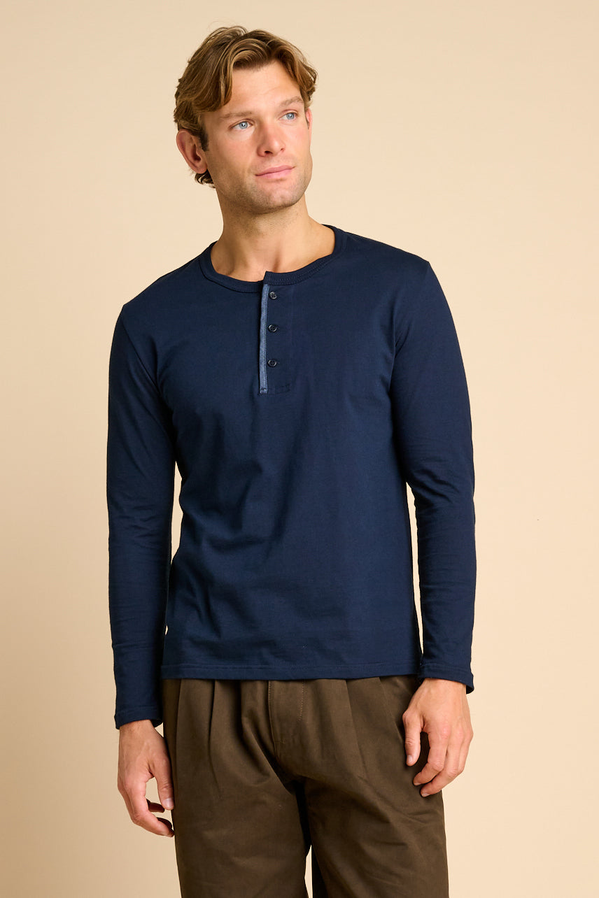 Man wearing a navy long-sleeve shirt and brown pants on a beige background.