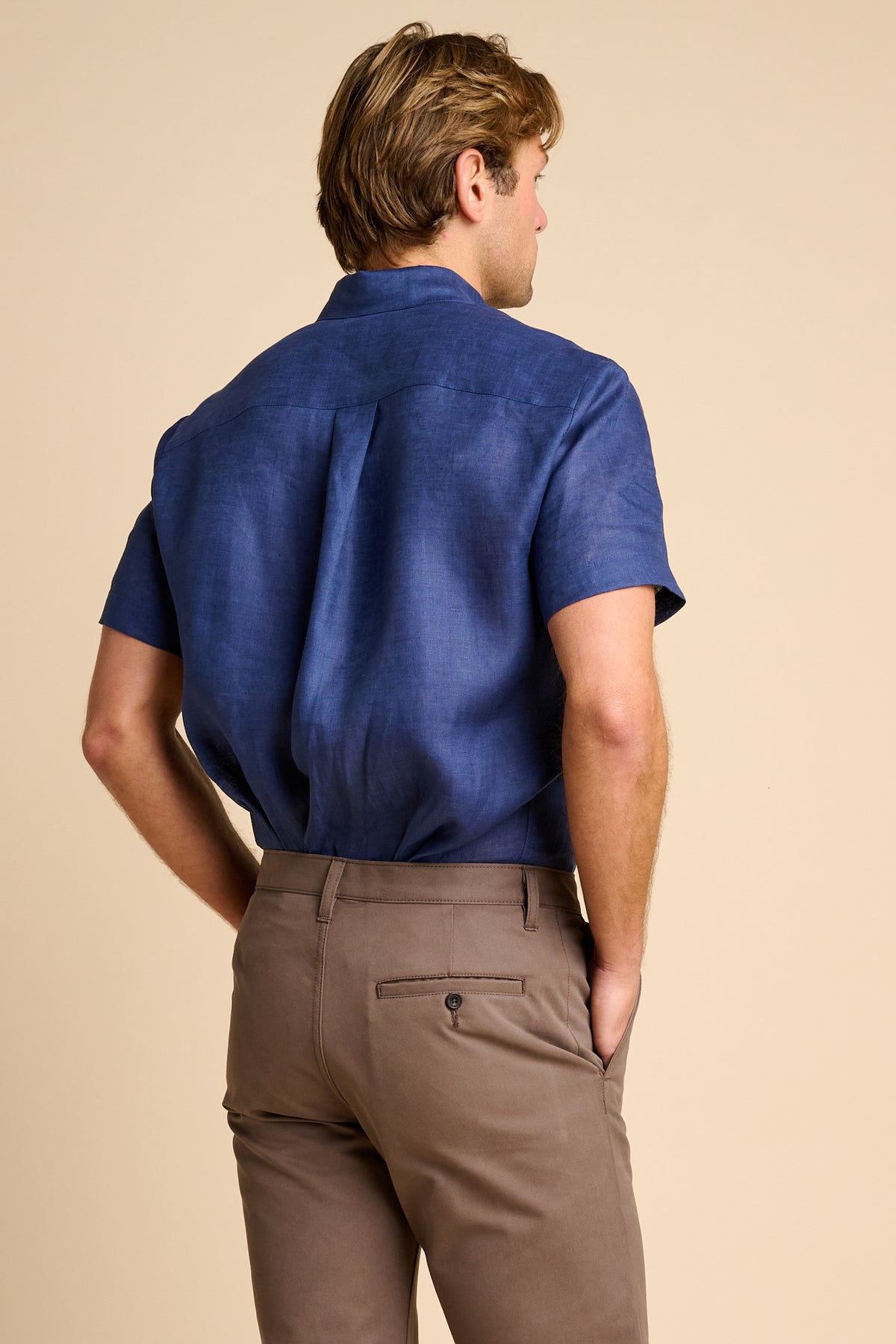 Man wearing brown pants and a blue shirt on a beige background.