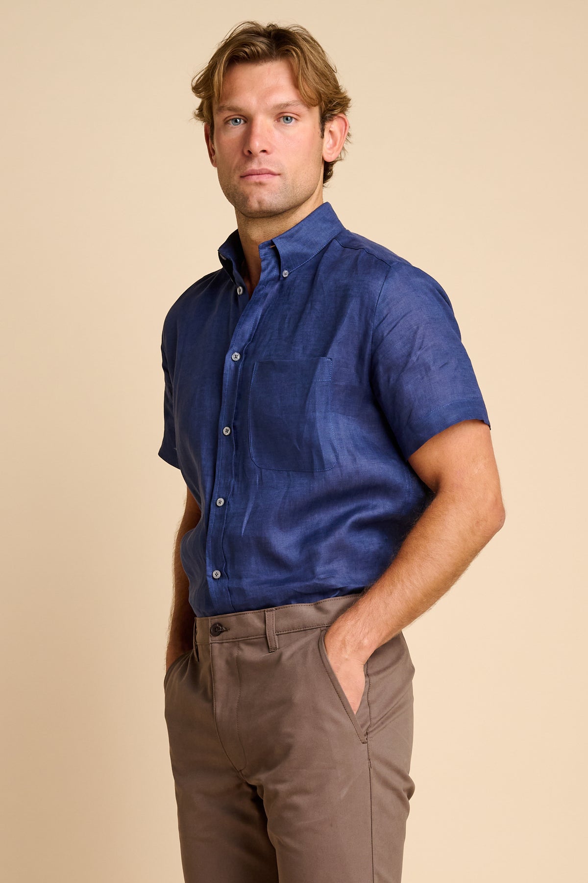 Man wearing a blue short-sleeve shirt and brown pants against a beige background