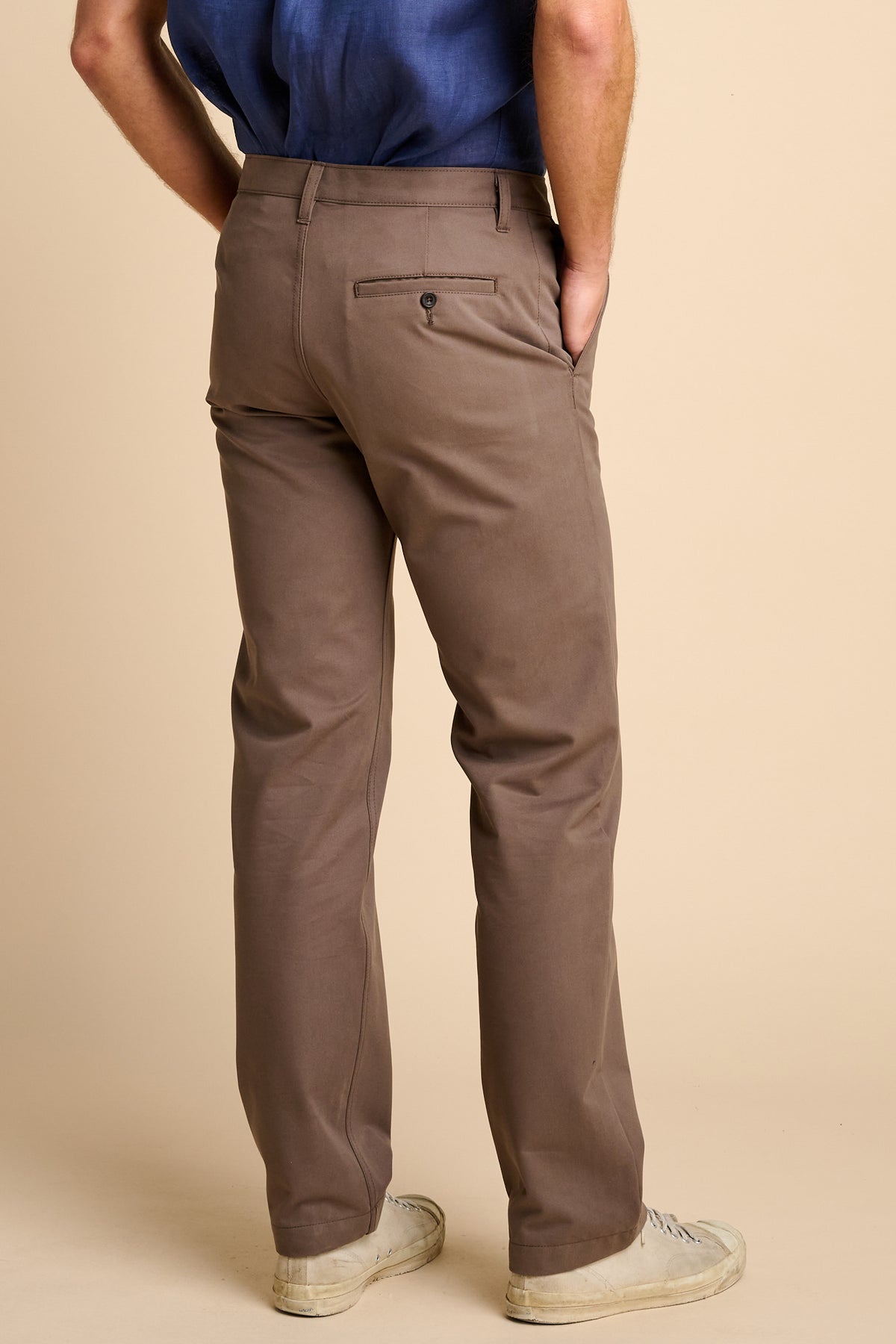 Man wearing brown pants and a blue shirt on a beige background.