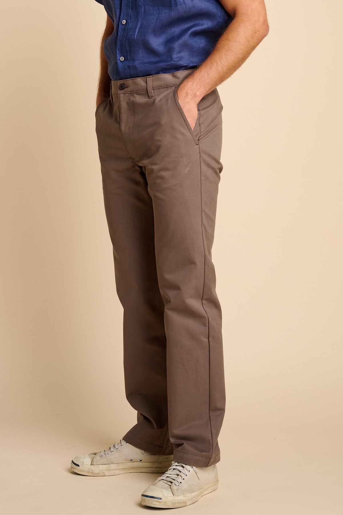 Person wearing brown pants and a blue shirt on a beige background