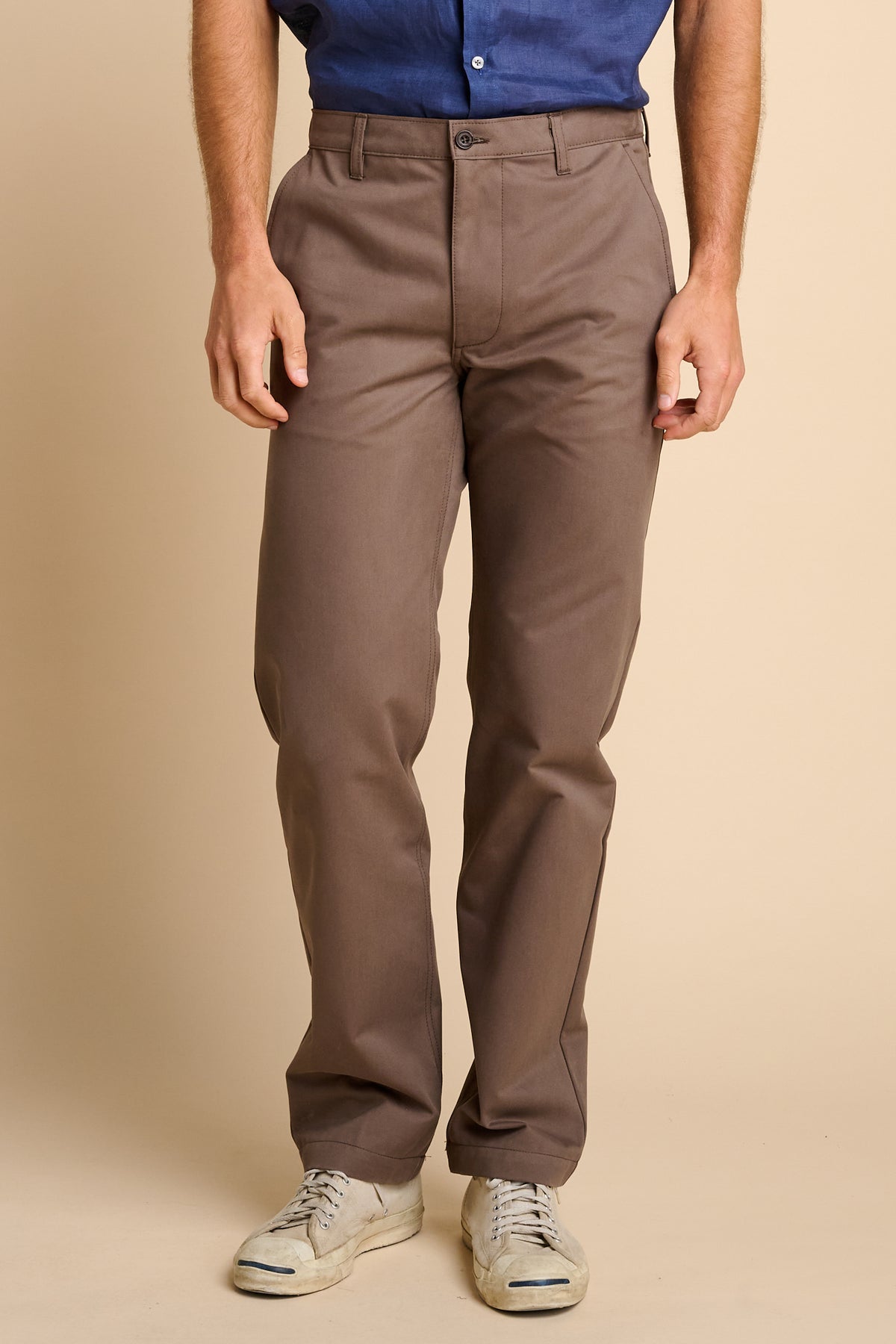Man wearing brown pants and a blue shirt on a beige background.