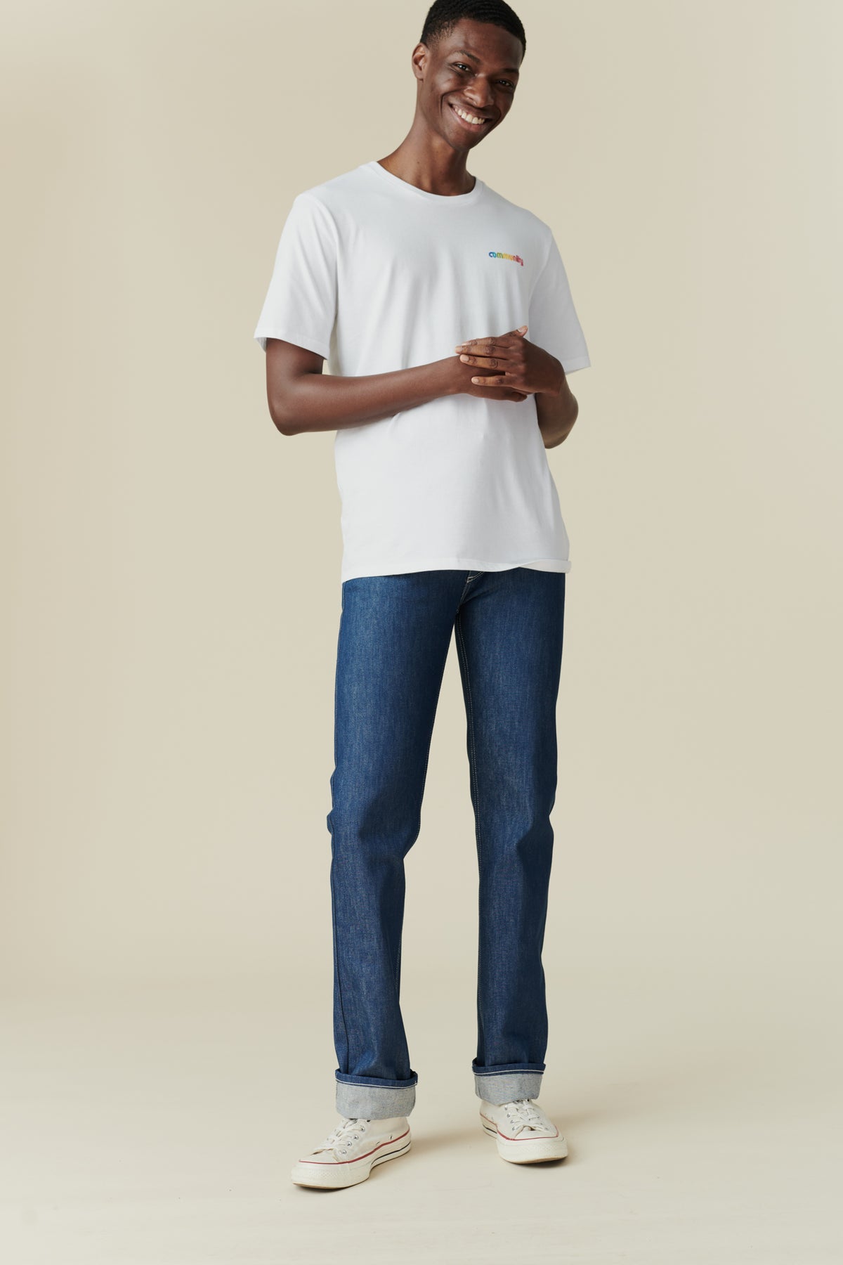 Full body front image of black male wearing straight cut jeans in blue, rolled hem. 