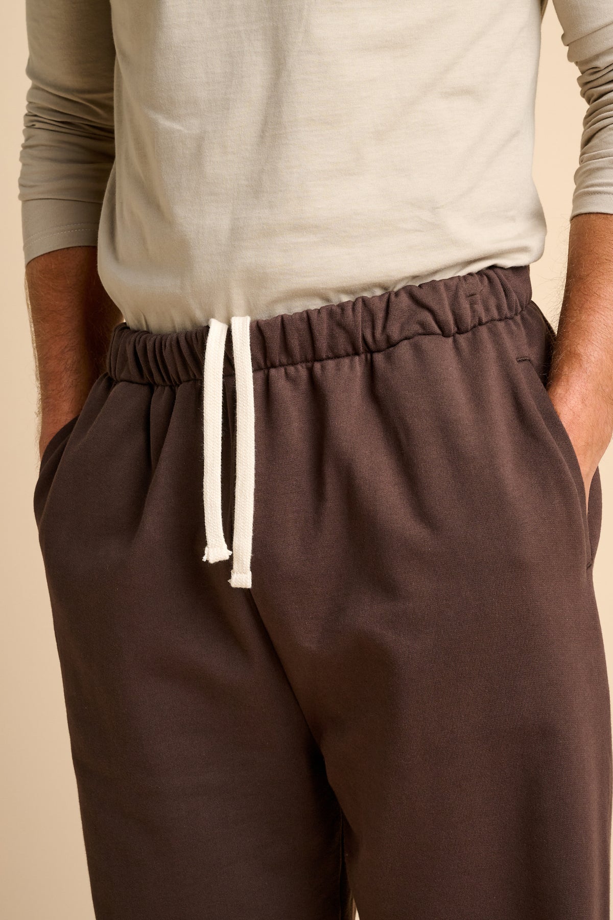 Chocolate brown sweatpants with a white drawstring on a beige background.