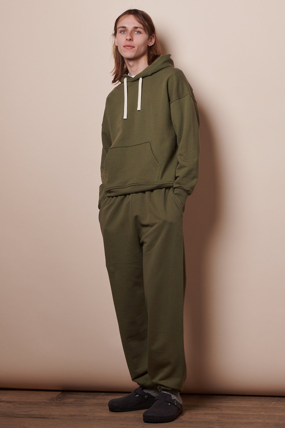 Full body image of male wearing sweatpants in olive paired with the matching hooded sweatshirt in olive