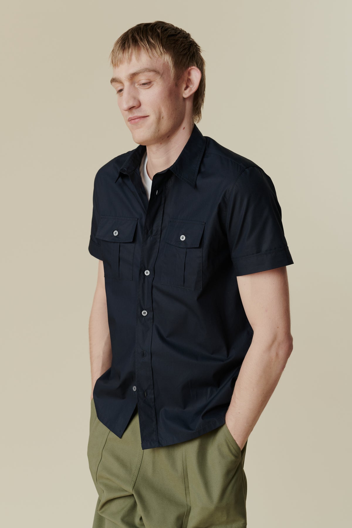 thigh up image of male wearing buttoned tom short sleeve military shirt with hands in pocket of cameraman pants in olive