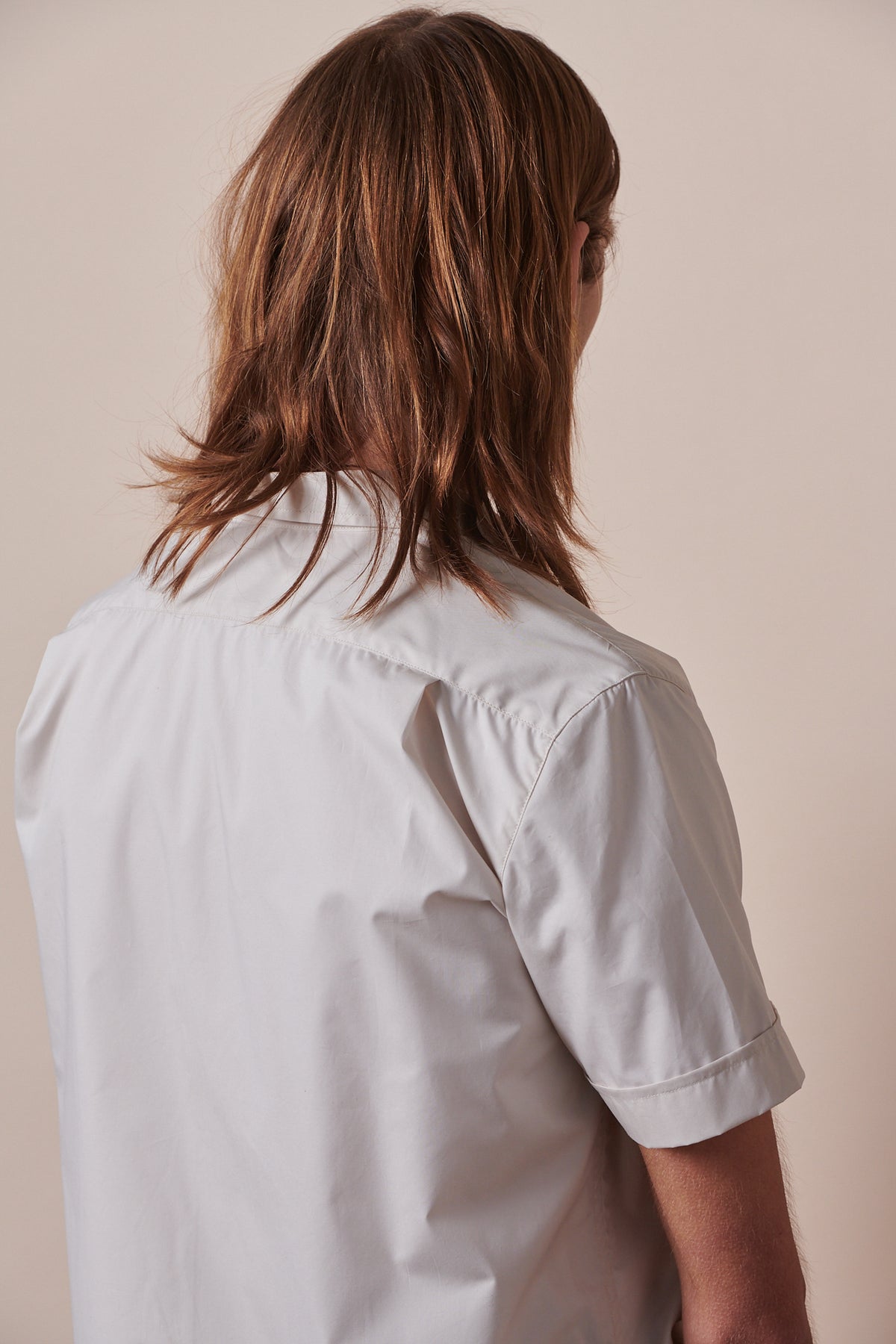Back of male with shoulder length hair wearing Tom short sleeve military shirt in stone 