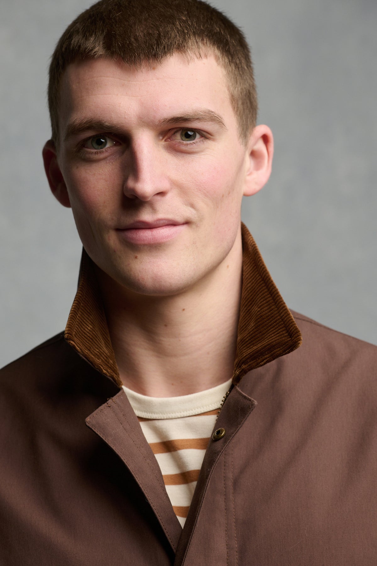 Portrait of brunet male wearing barn jacket in brown with brown cord collar up, worn over men's Breton in ecru cinnamon