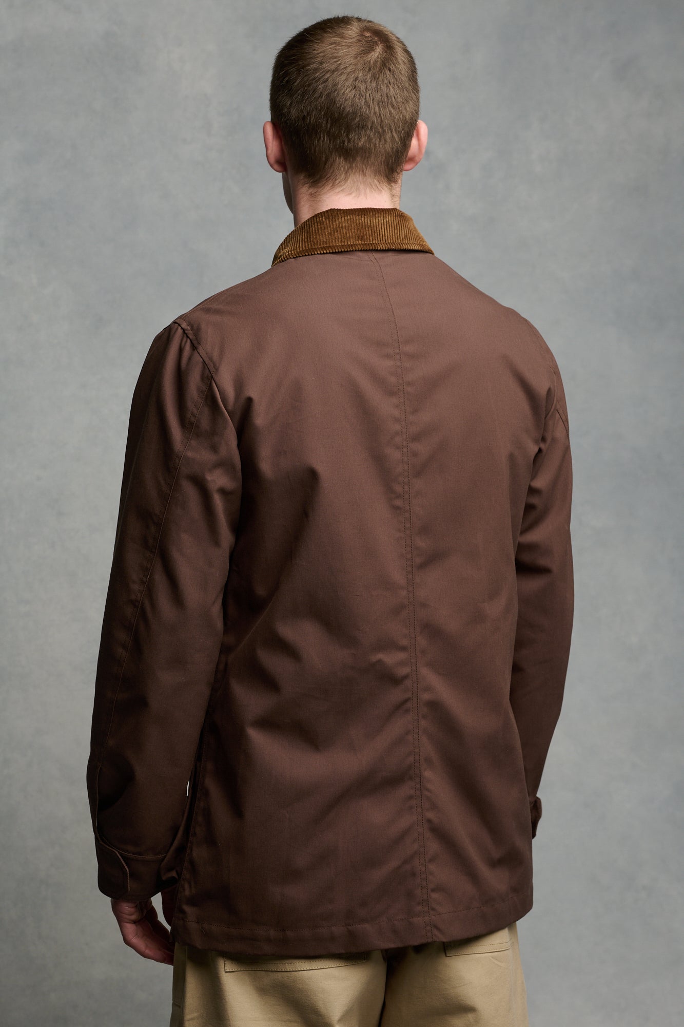 Thigh up image of male wearing men's barn jacket in brown unzipped over Breton in ecru cinnamon paired with cameraman pant in putty